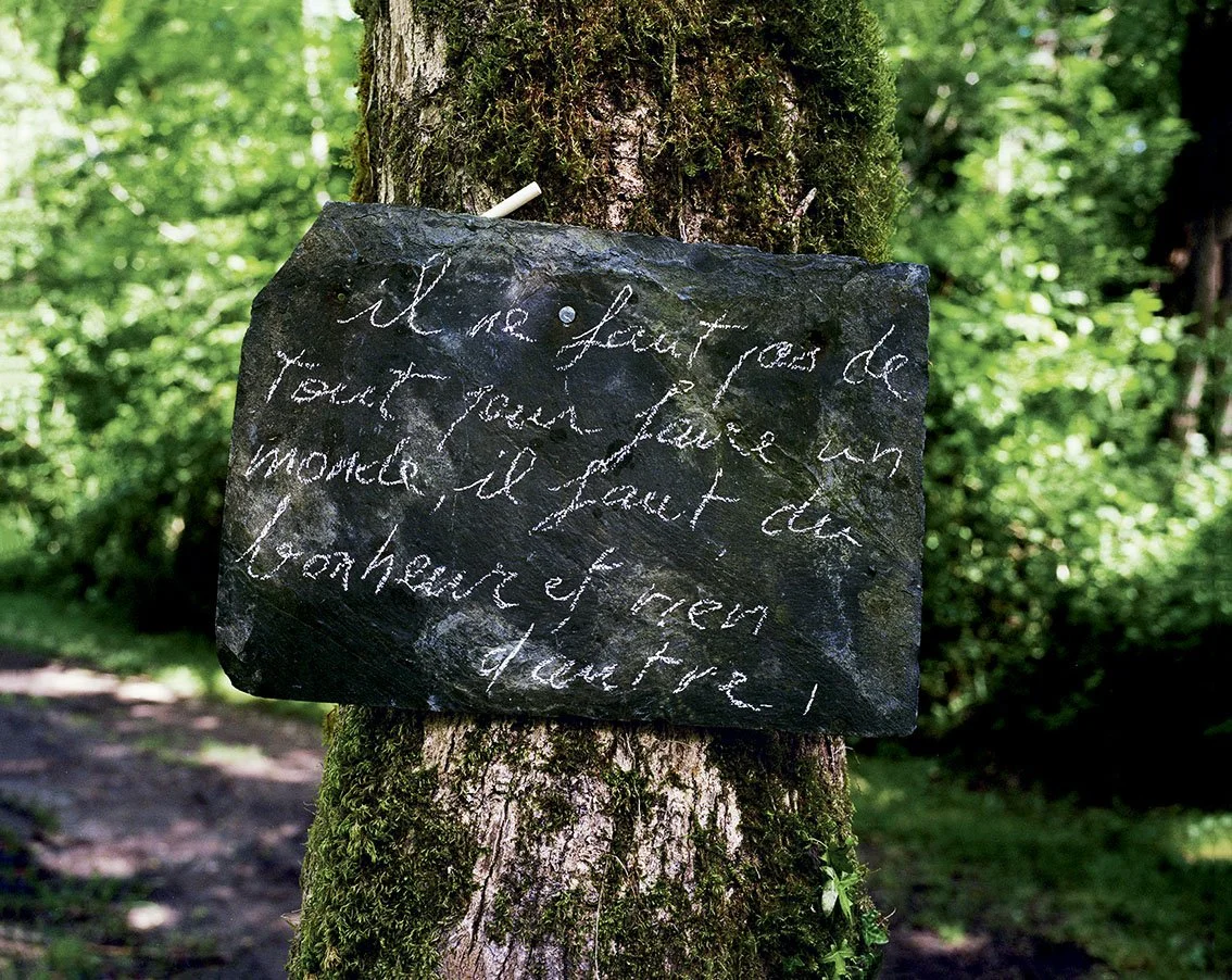 Slate plaque attached to a tree with a quotation written in French, in a verdant forest setting.