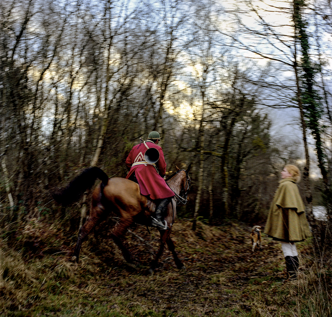 Homme en uniforme d'époque à cheval dans une forêt, femme en manteau regardant, avec un chien à ses côté.