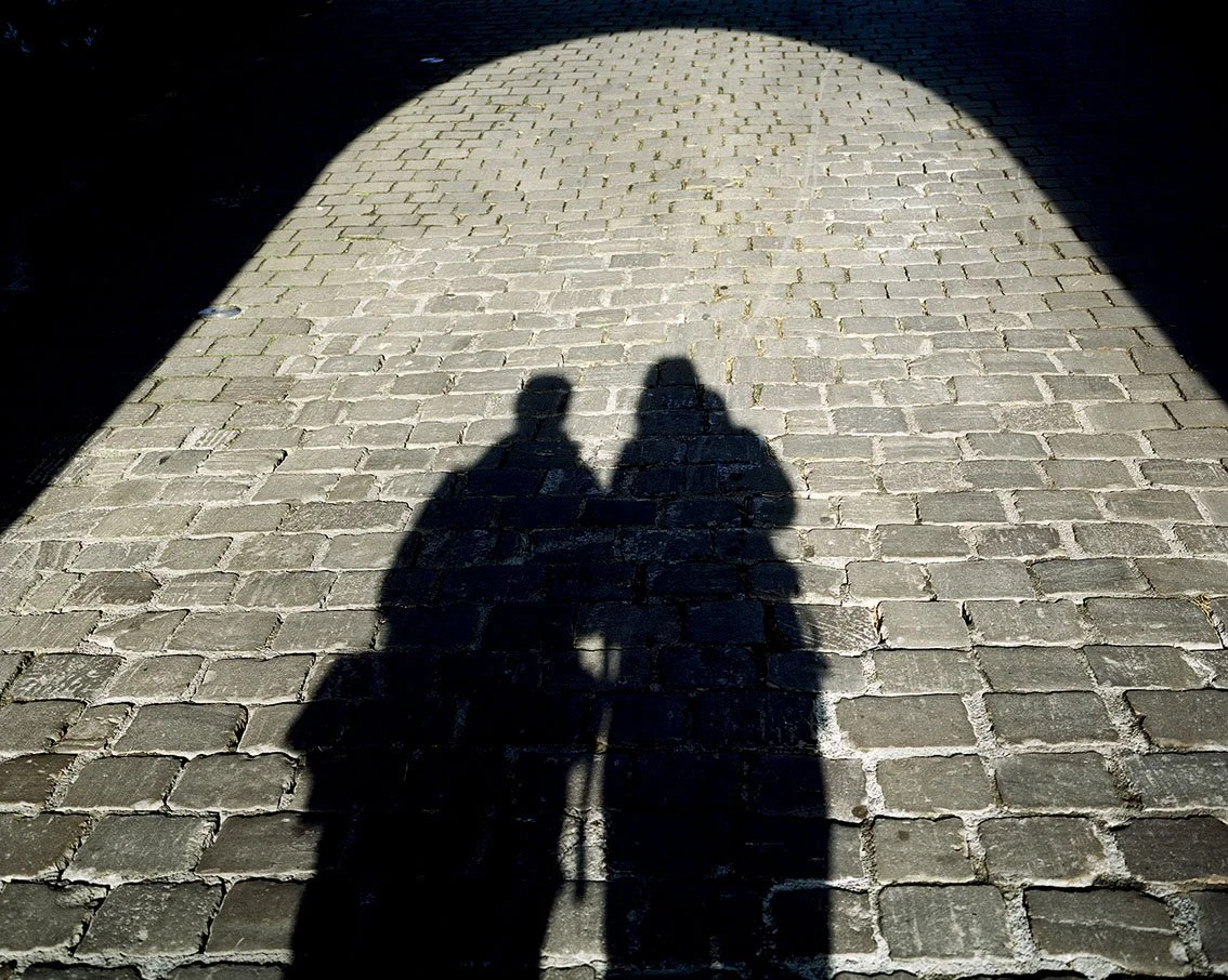Shadows of two people on a cobblestone sidewalk, with a large circle of light above.