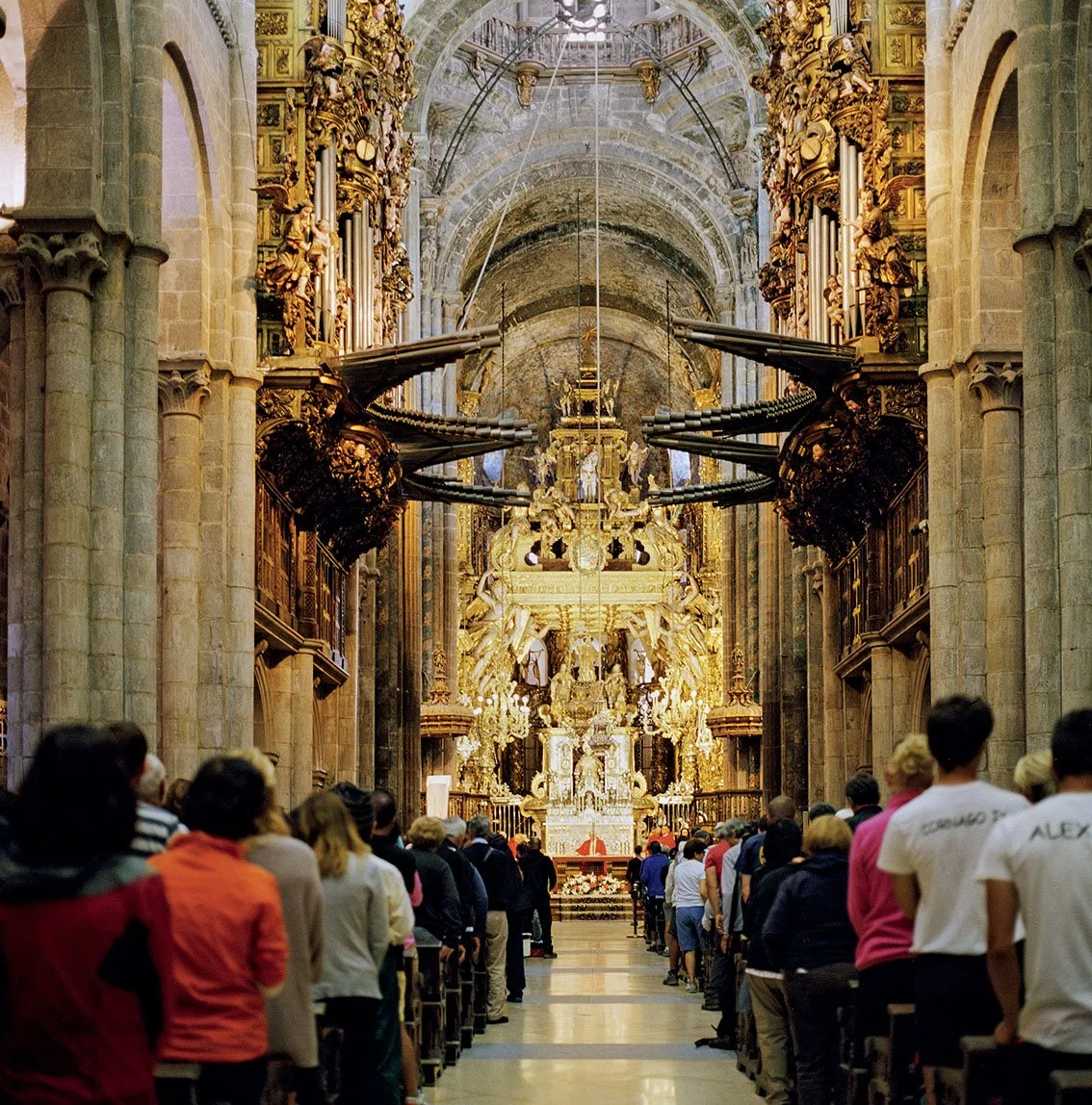 Interior of a Baroque church adorned with gilded details, with people queuing to enter or take part in a religious ceremony.