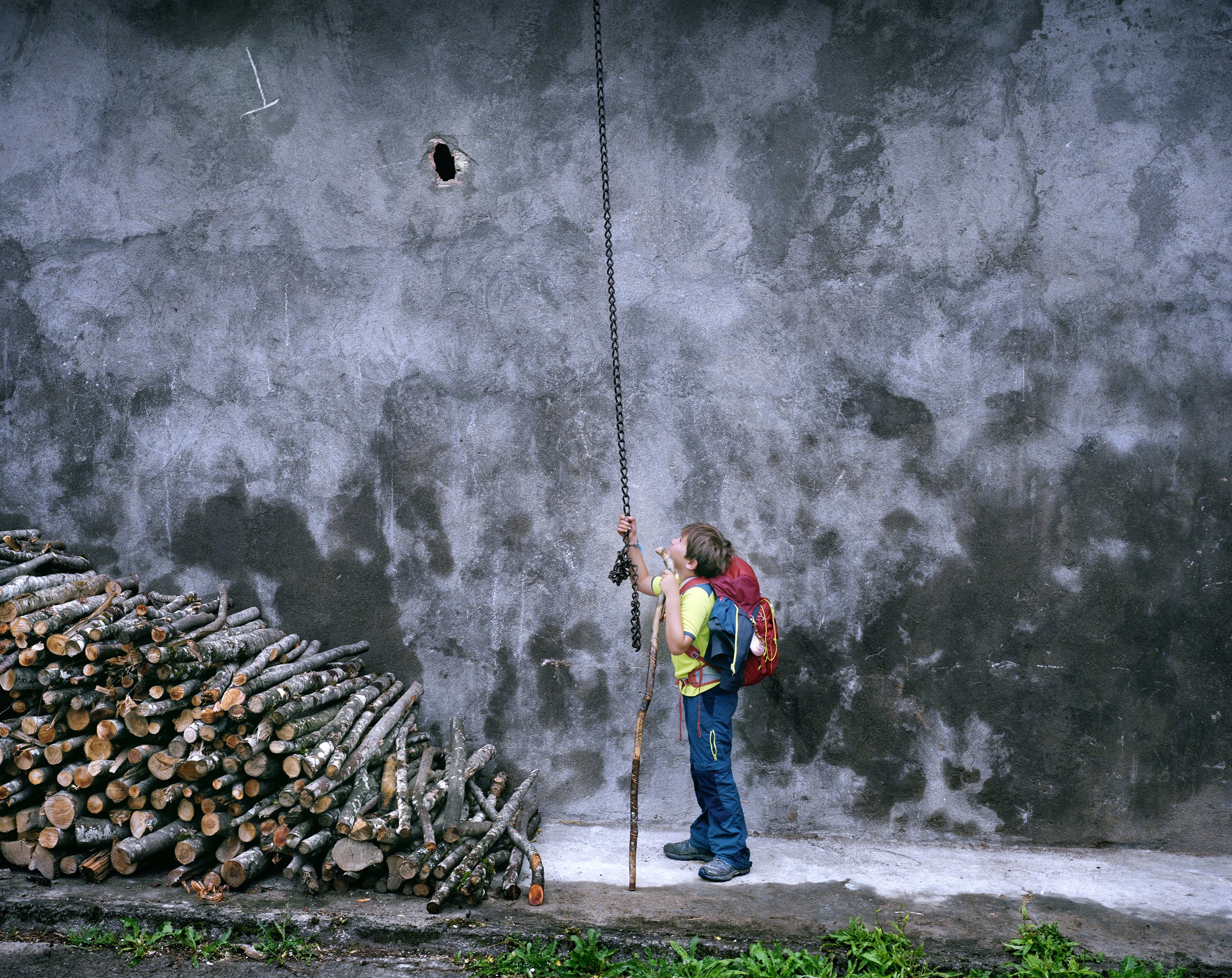 A person with a growing backpack looking at a chain hanging in front of a concrete wall.