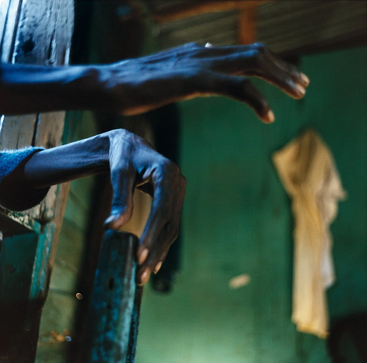 Carved wooden hands clinging to a wooden surface, interior with green wall and beige cloth garment hanging on the wall.