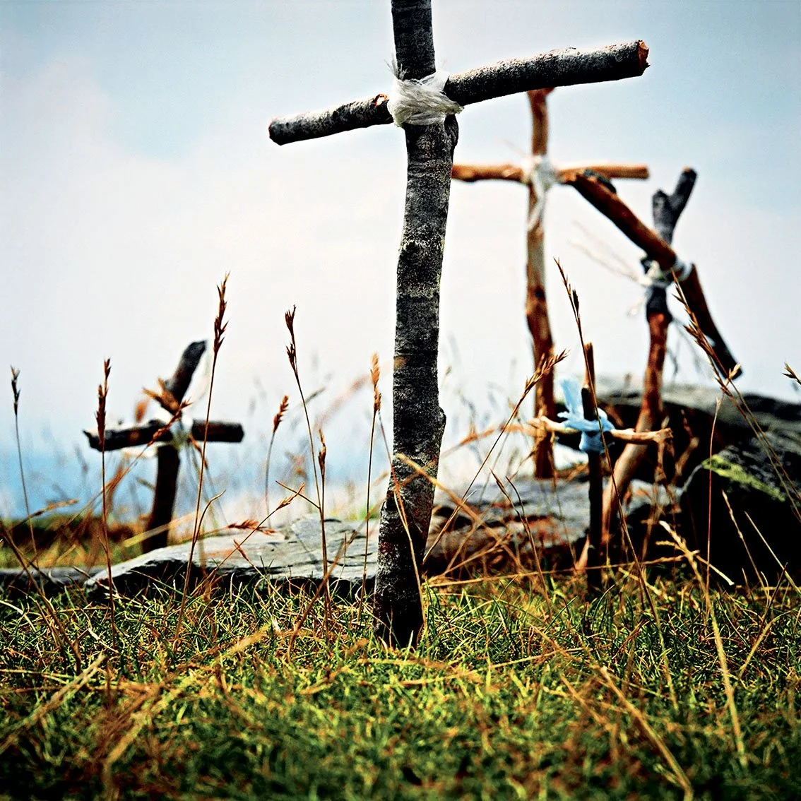 Handcrafted wooden cross on a grassy field with other small wooden crosses in the background.