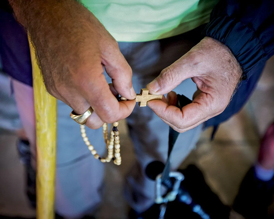 Two hands of an elderly person holding a wooden crucifix and a rosary.