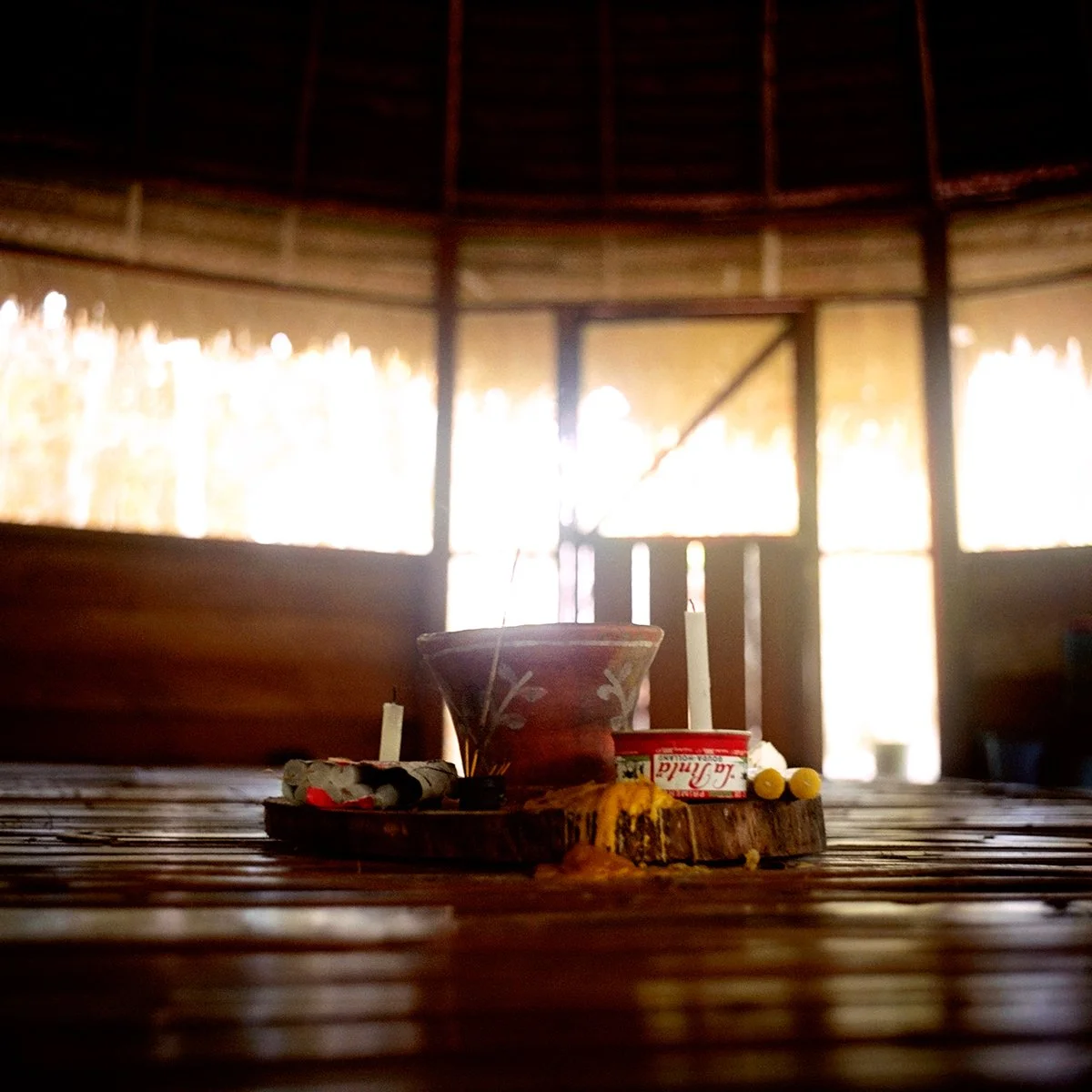 A wooden table with decoration in a wooden room, lit by natural light behind. On the table is a terracotta pot surrounded by candles and other small objects.