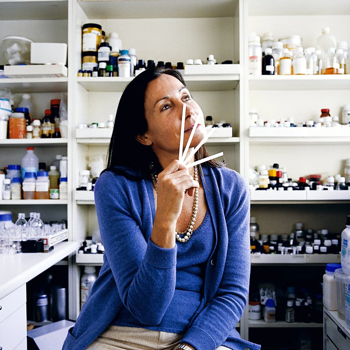 A woman in a pharmacy or laboratory, holding ribbons of different colors, gazing pensively.