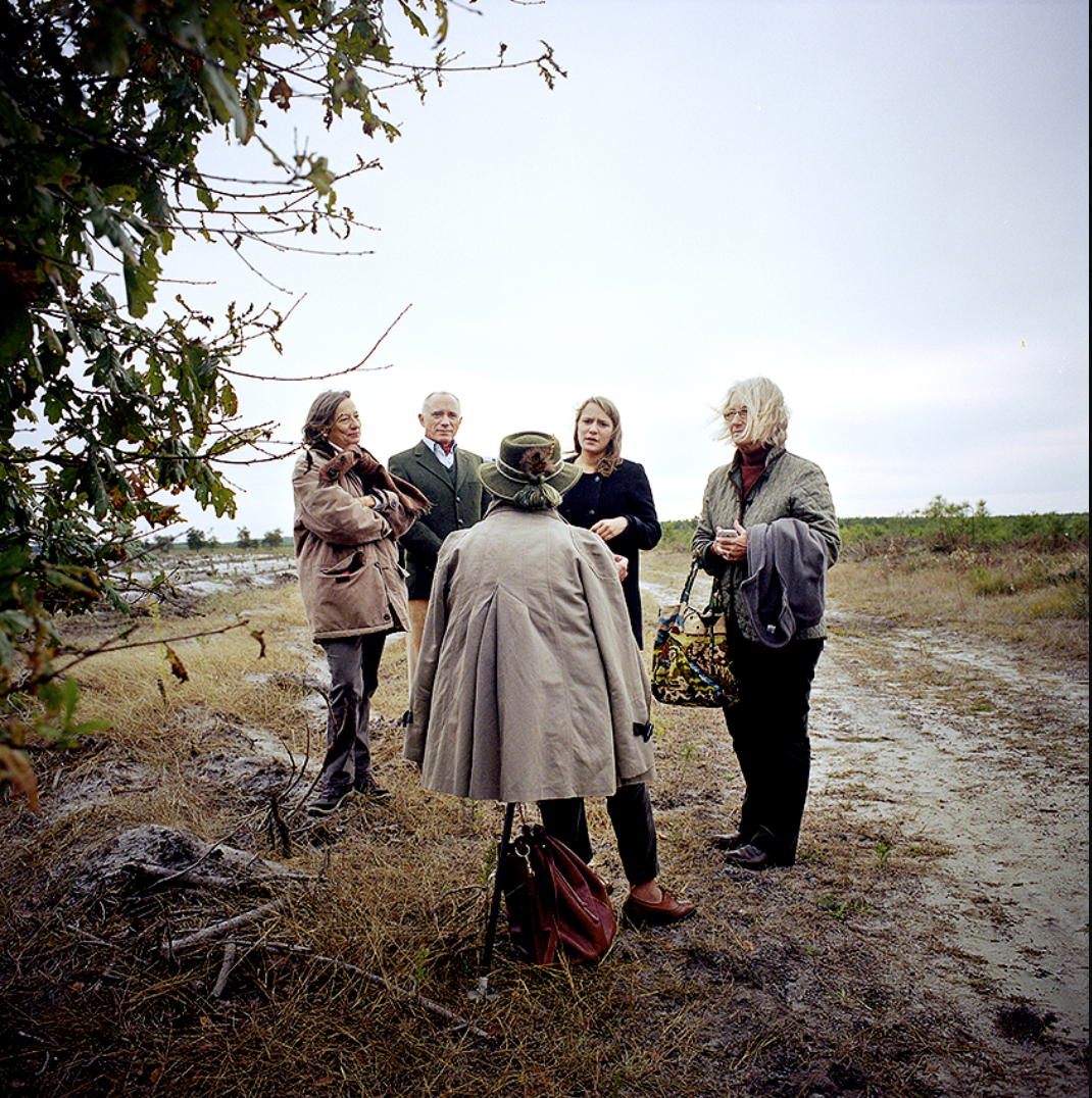 Un groupe de cinq personnes en conversation dans un paysage extérieur, avec un sentier de terre et des arbres en arrière-plan.