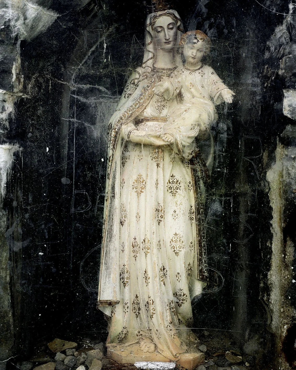 Stone statue of the Virgin Mary holding the Infant Jesus, set in a rocky setting with signs of cleaning or ageing.