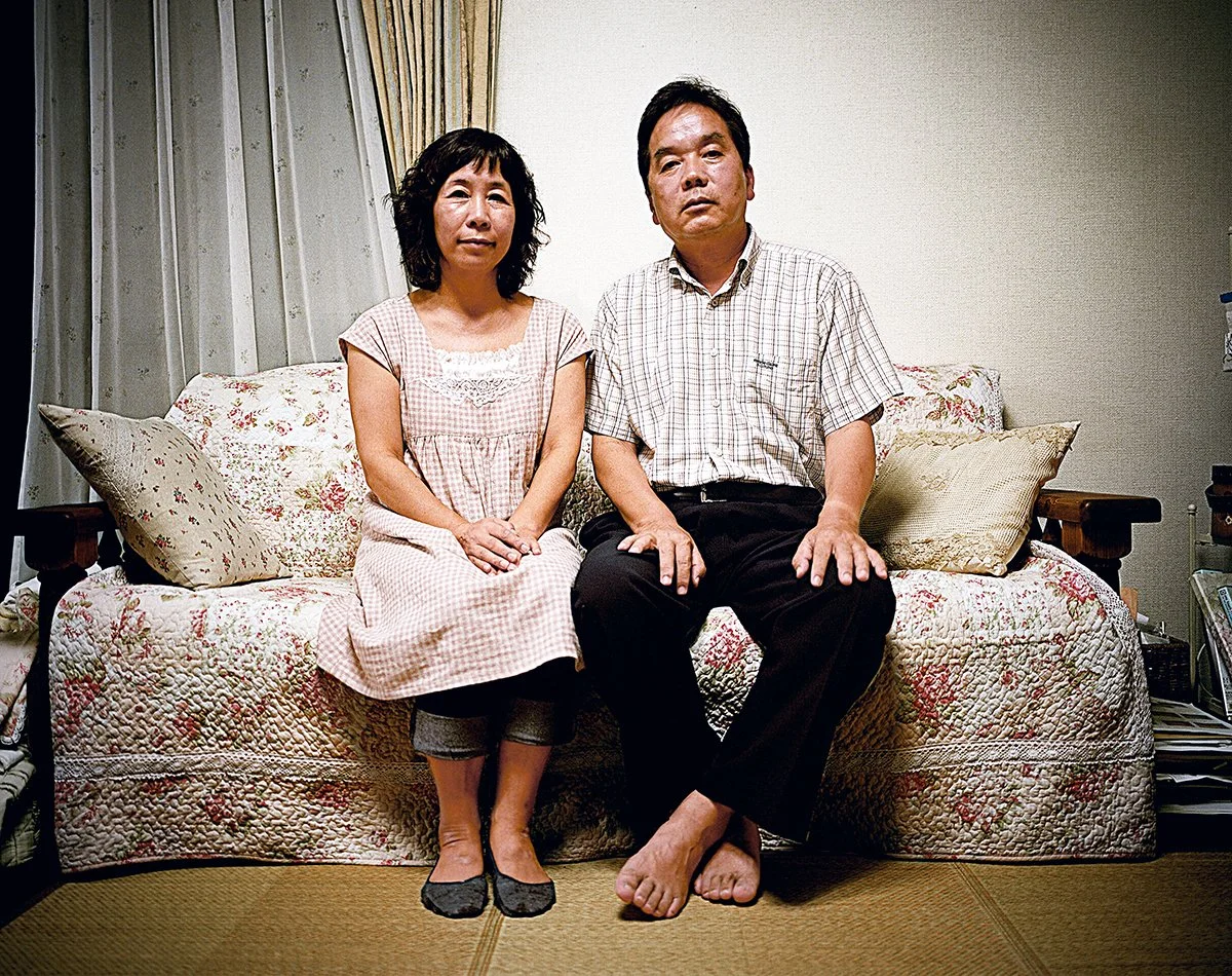 Un homme et une femme assis côte à côte sur un canapé dans une pièce, regardant vers l'appareil photo.