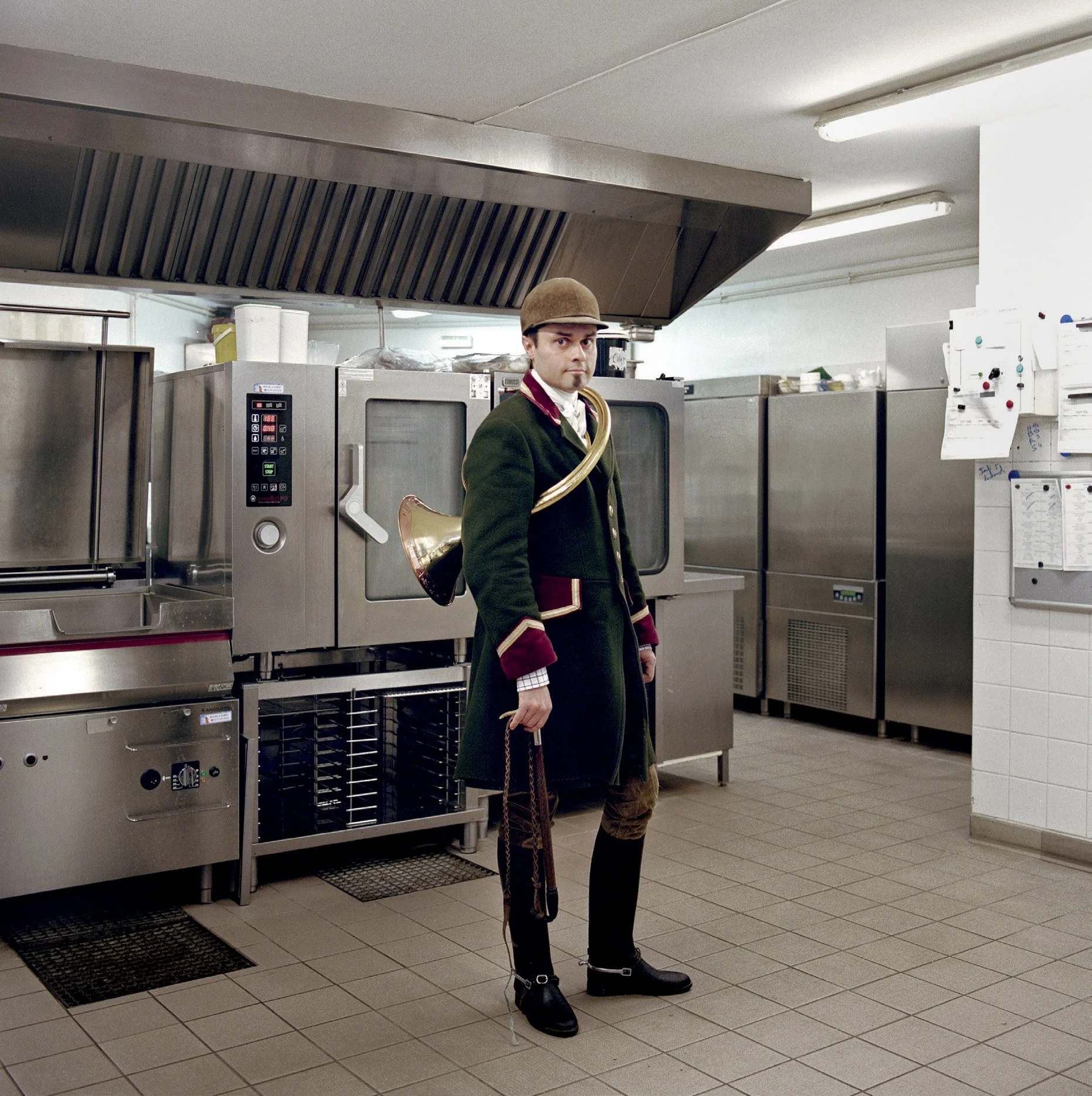 A man dressed as a weeping pip in an industrial kitchen, wearing a traditional Scottish sheepskin suit, tweed hat and bagpipes on his back.