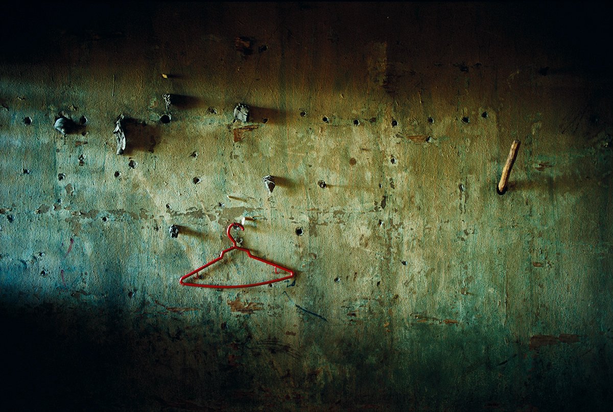 A decrepit wall with holes, a wooden hook and a red coat hanger hanging from a nail, a dark, abandoned atmosphere.