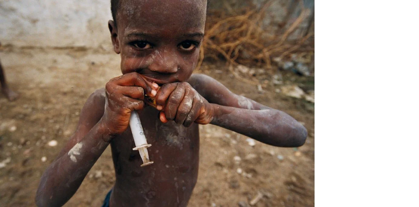 Jeune garçon avec une seringue, dans un environnement pauvre, semblant injecter une substance à son bras.