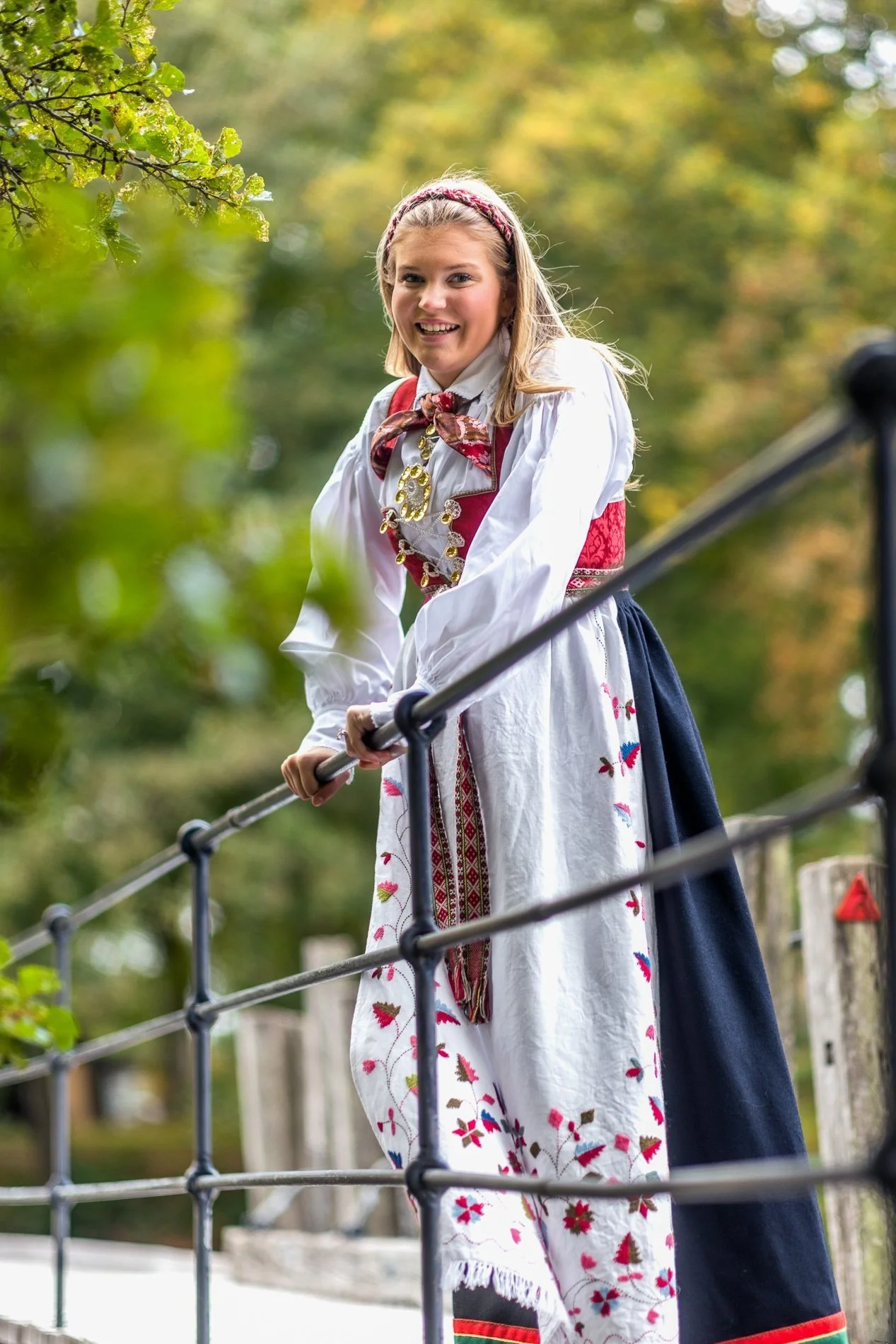 En kvinne i traditionell norsk bunad leker foran en barriere i en utendørspark.