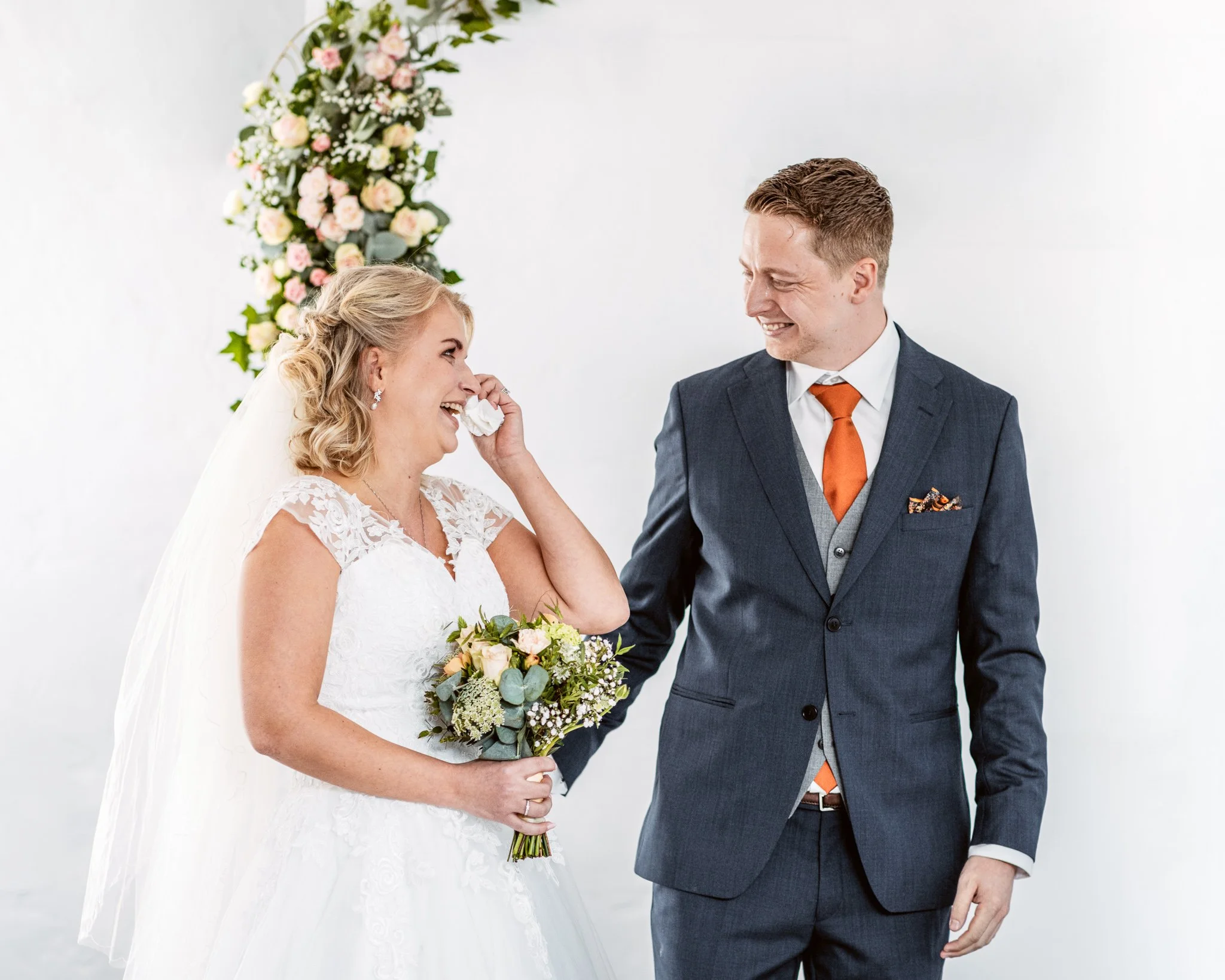 Et lesbisk brudepar ler og deler en emosjonell stund under vielsen, med en blomsterdekorasjon i bakgrunnen.