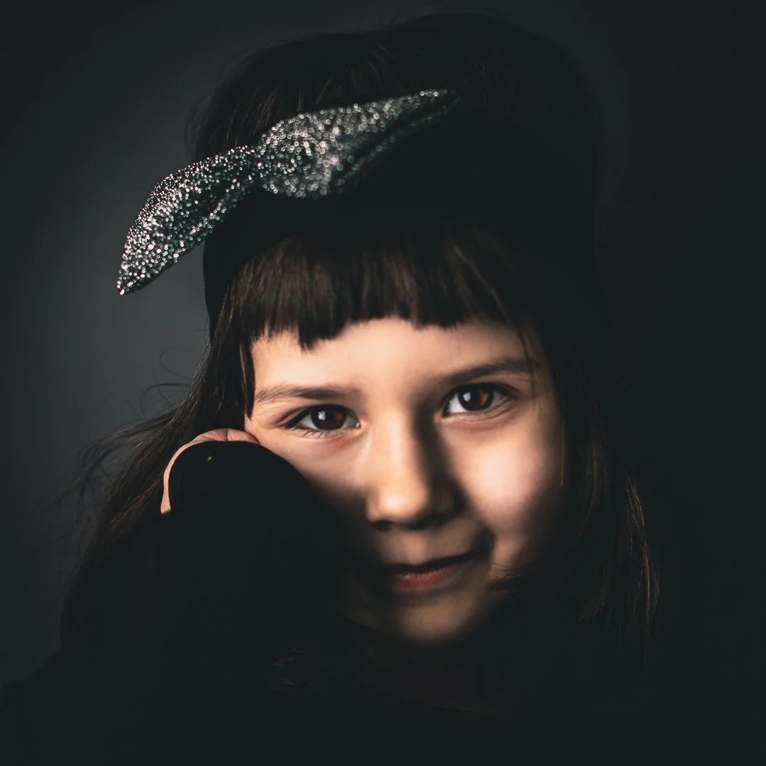 Portrett av en ung jente med kort svart hår, iført en glitrende hodebånd, mot en mørk bakgrunn.