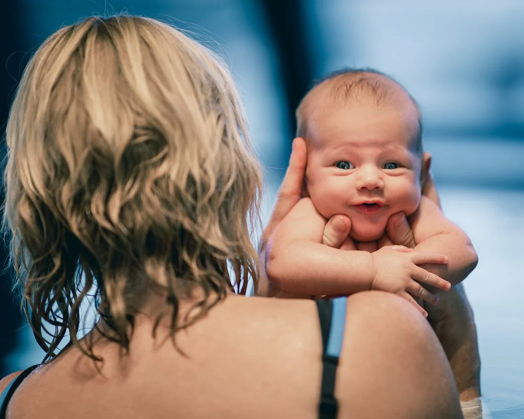 En kvinne med blond, krøllete hår holder en baby som ser overrasket ut.