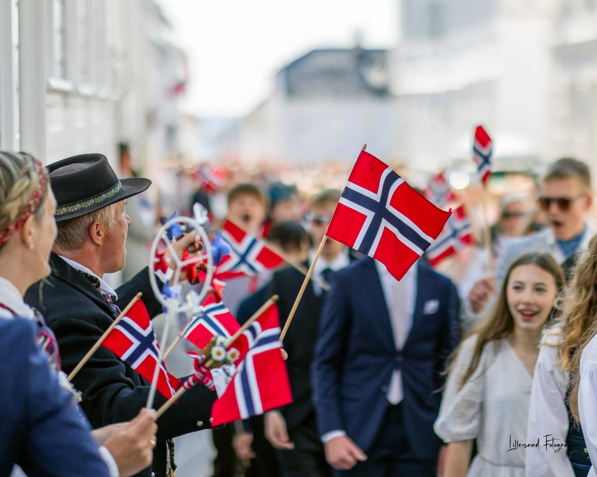 Feiring med norske flagg og mennesker i festantrekk, sannsynligvis ved en nasjonaldag, på gaten i Norge