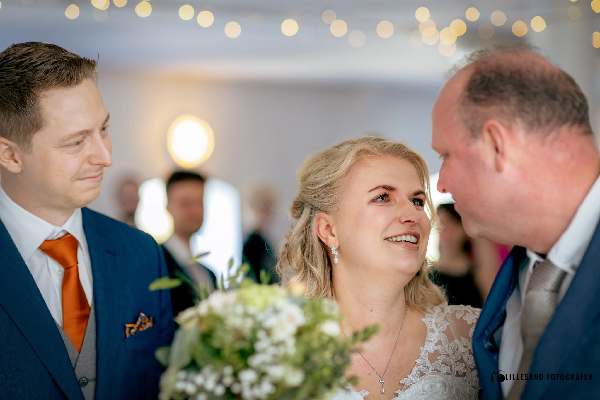 En bryllupsseremoni med en brud, en brudgom og en annen mann, i et festlokale med hengende lys.