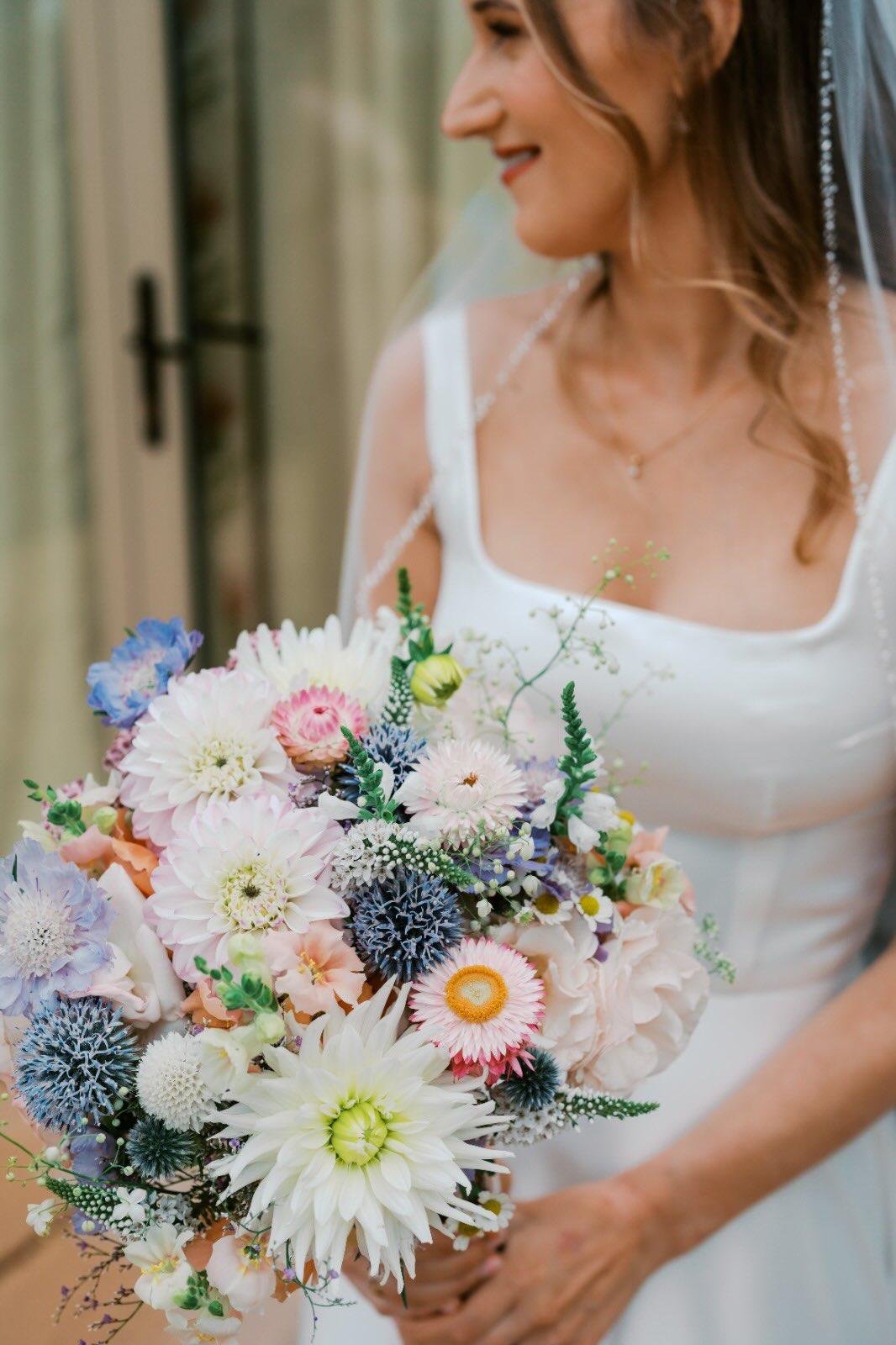 A woman in a white dress holding a colorful bouquet of flowers, smiling.