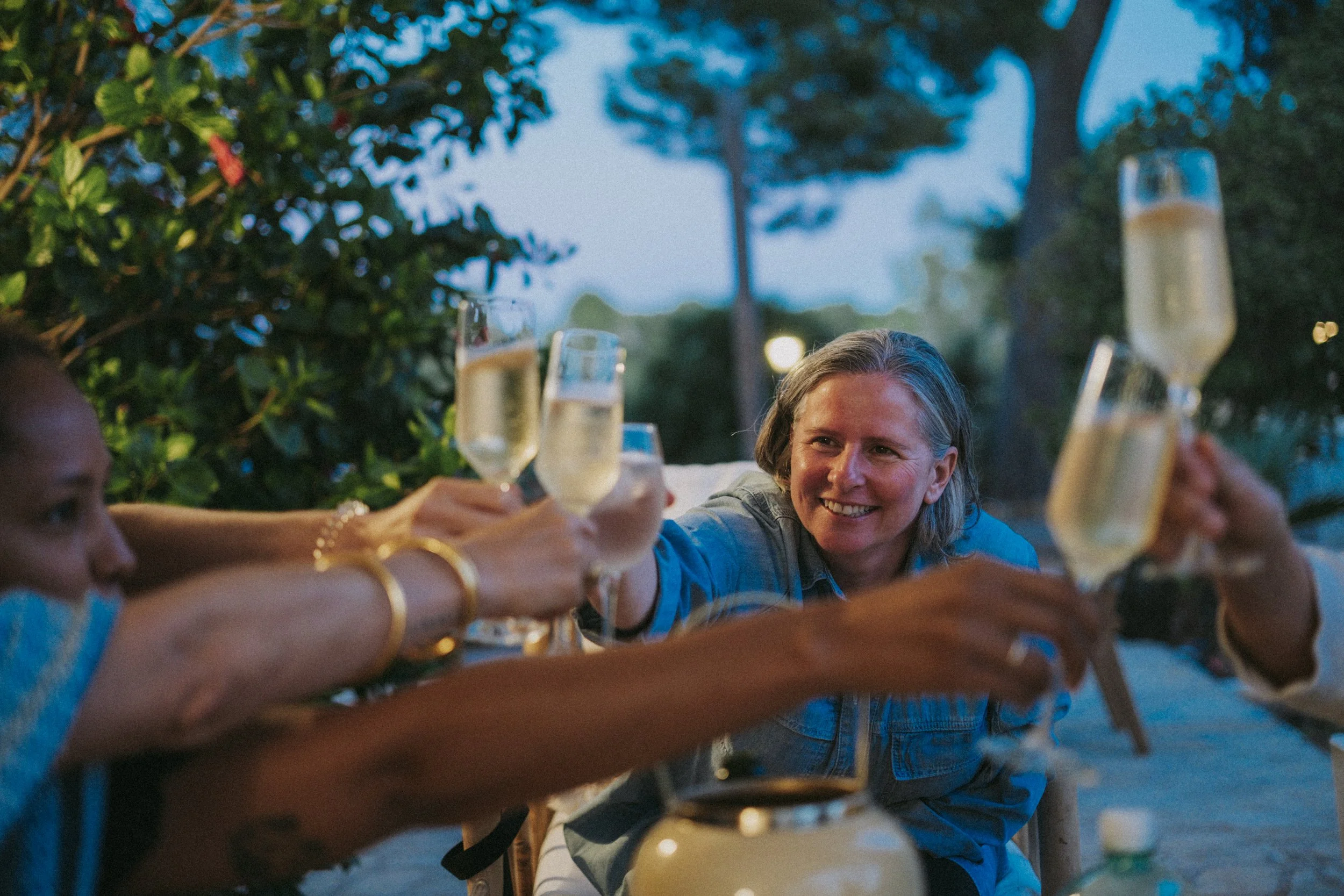 People raising champagne glasses in a toast outdoors during the evening, smiling and celebrating.