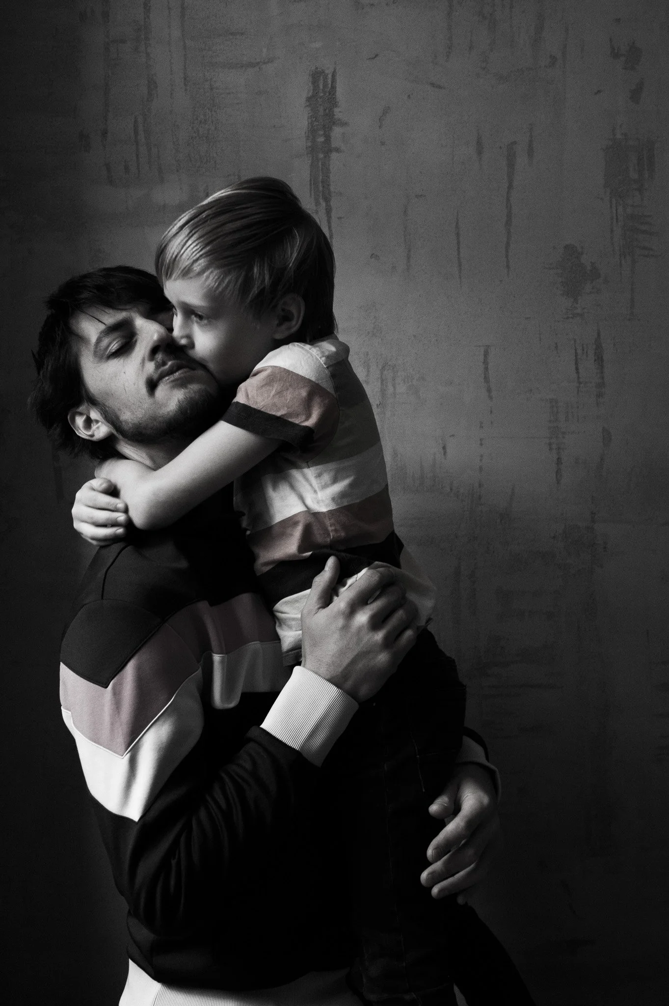 Schwarzweißfoto eines Mannes, der einen jungen Jungen in den Armen hält, während der Junge dem Mann einen Kuss auf die Wange gibt.
