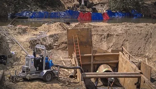 Construction worker pouring concrete on a sidewalk with a concrete finishing tool nearby, construction equipment in the background.