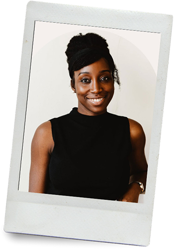 A smiling Black woman with styled hair, wearing a sleeveless black top, standing against a plain white background.