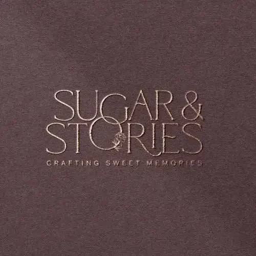 Close-up of a dark brown textured surface with the embossed text 'SUGAR & STORIES' and the tagline 'CRAFTING SWEET MEMORIES.'