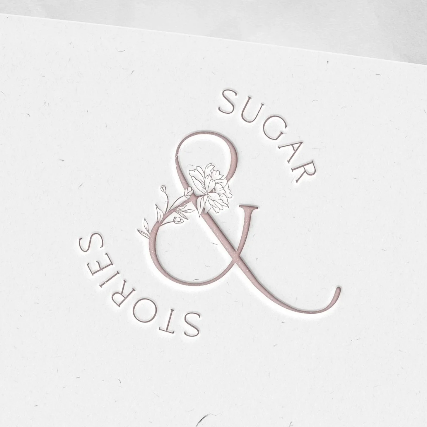 Close-up of a white card with a decorative gold ampersand and the words "SUGAR & STONES" arranged in a circle around it.