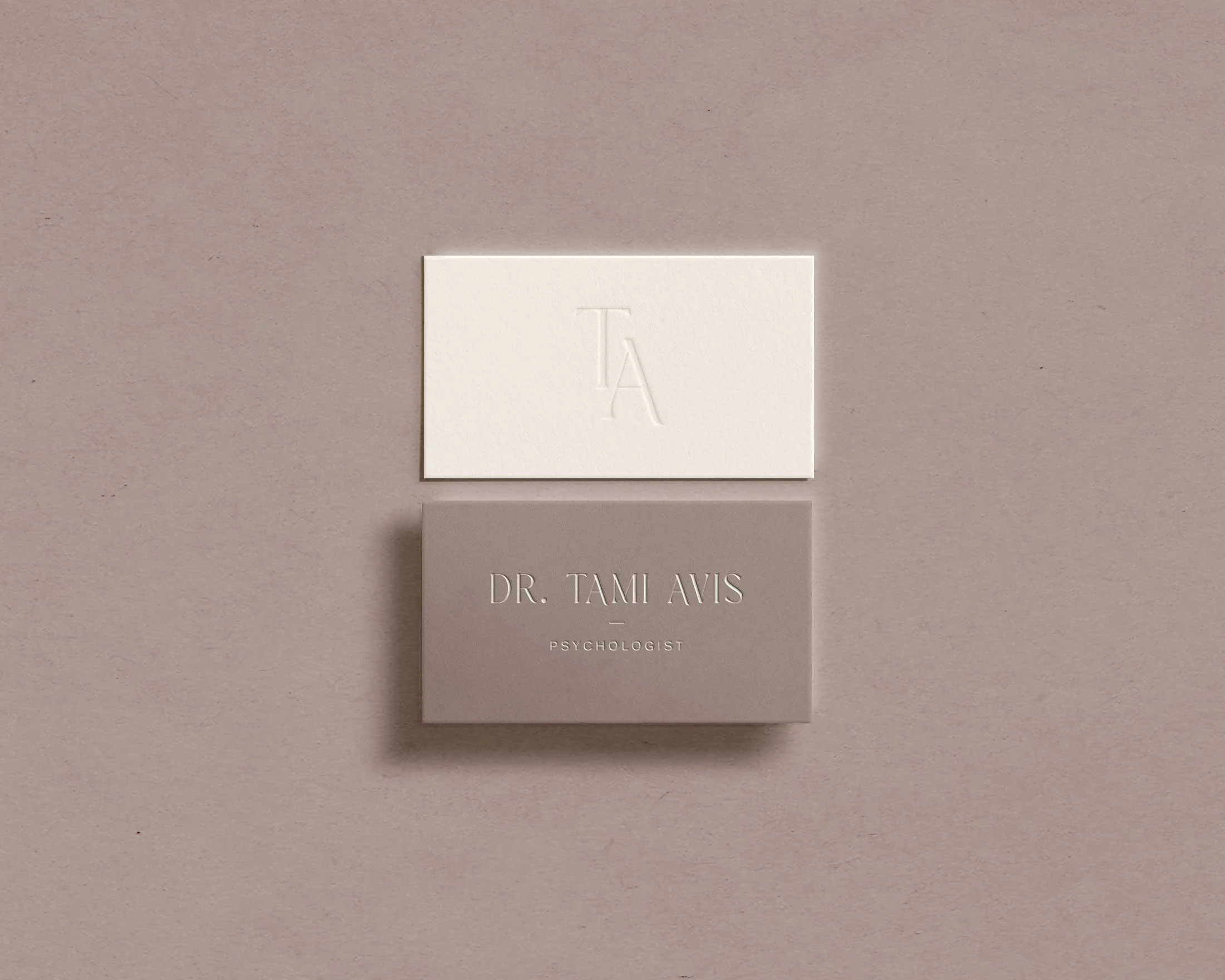 A white card with embossed letter A featuring a shadow, and below it, text reading 'DR. TAMI AVIS PSYCHOLOGIST', placed on a gray background.