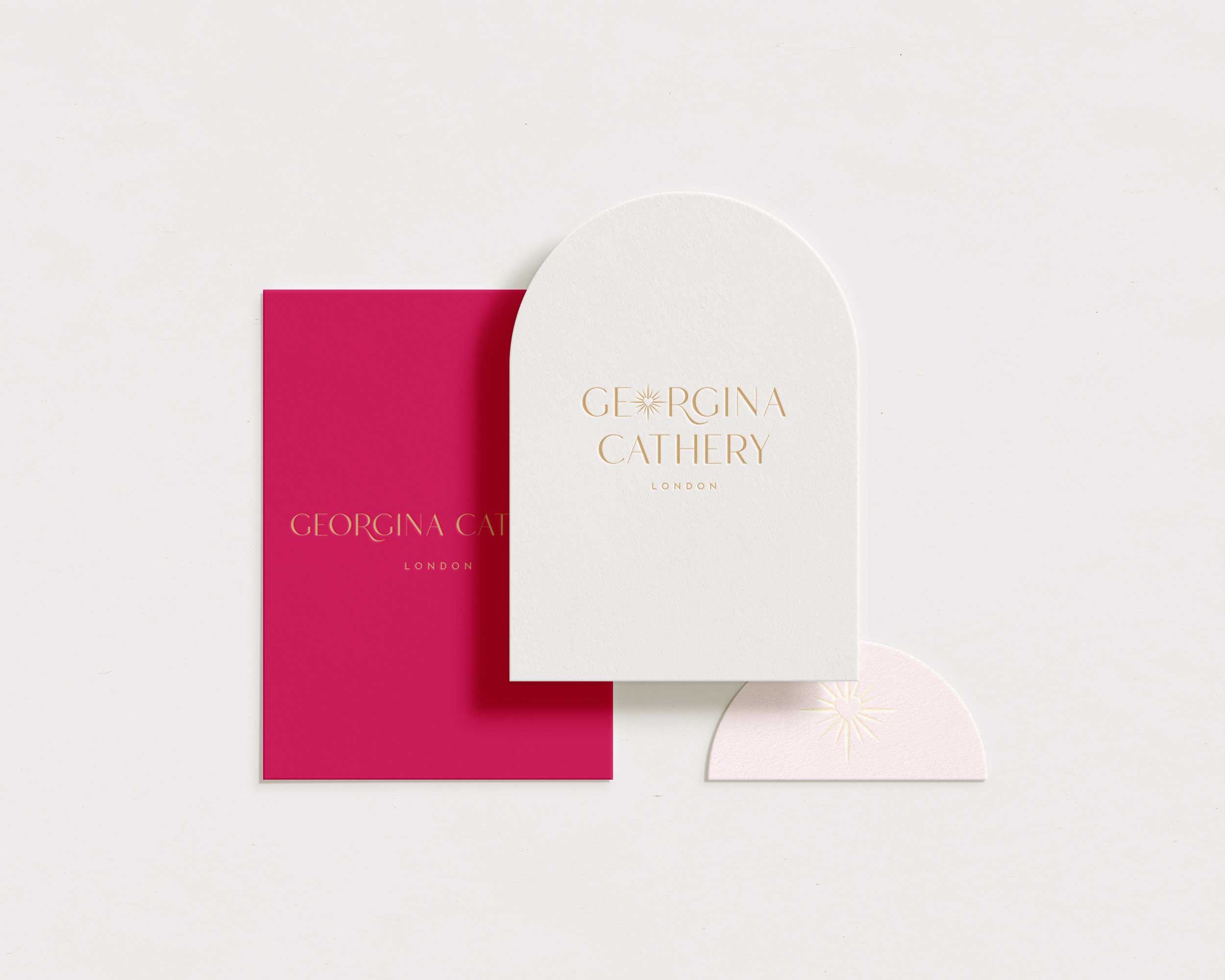 A white card with gold embossed text reading 'GEORGINA CATHERY LONDON' is placed over a frosted white circle and a bright pink rectangle on a plain white background.