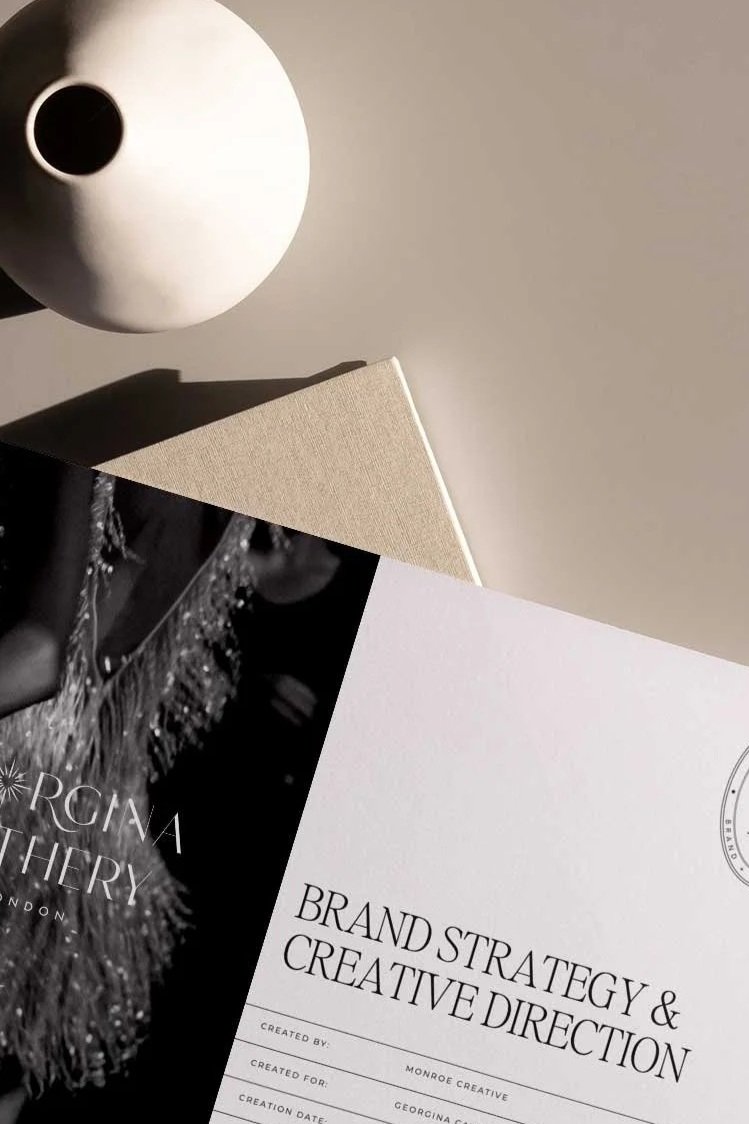 Flat lay of a white vase, beige notebook, and marketing plan documents on a neutral background.