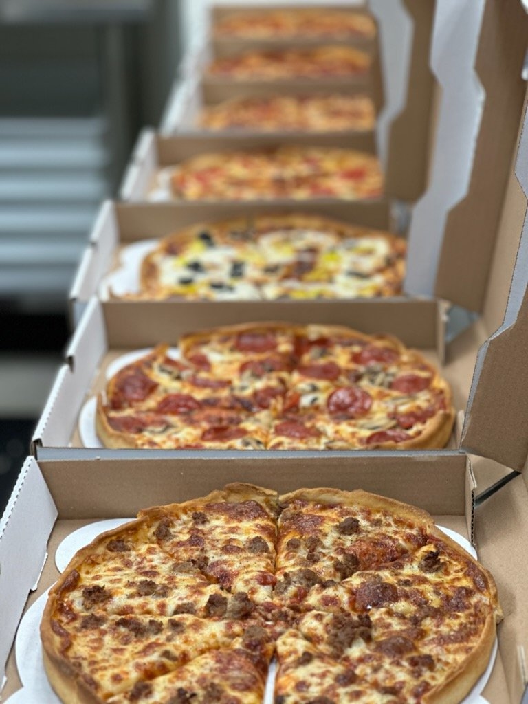 Multiple pizzas in open pizza boxes lined up in a row, with different toppings visible on each pizza.