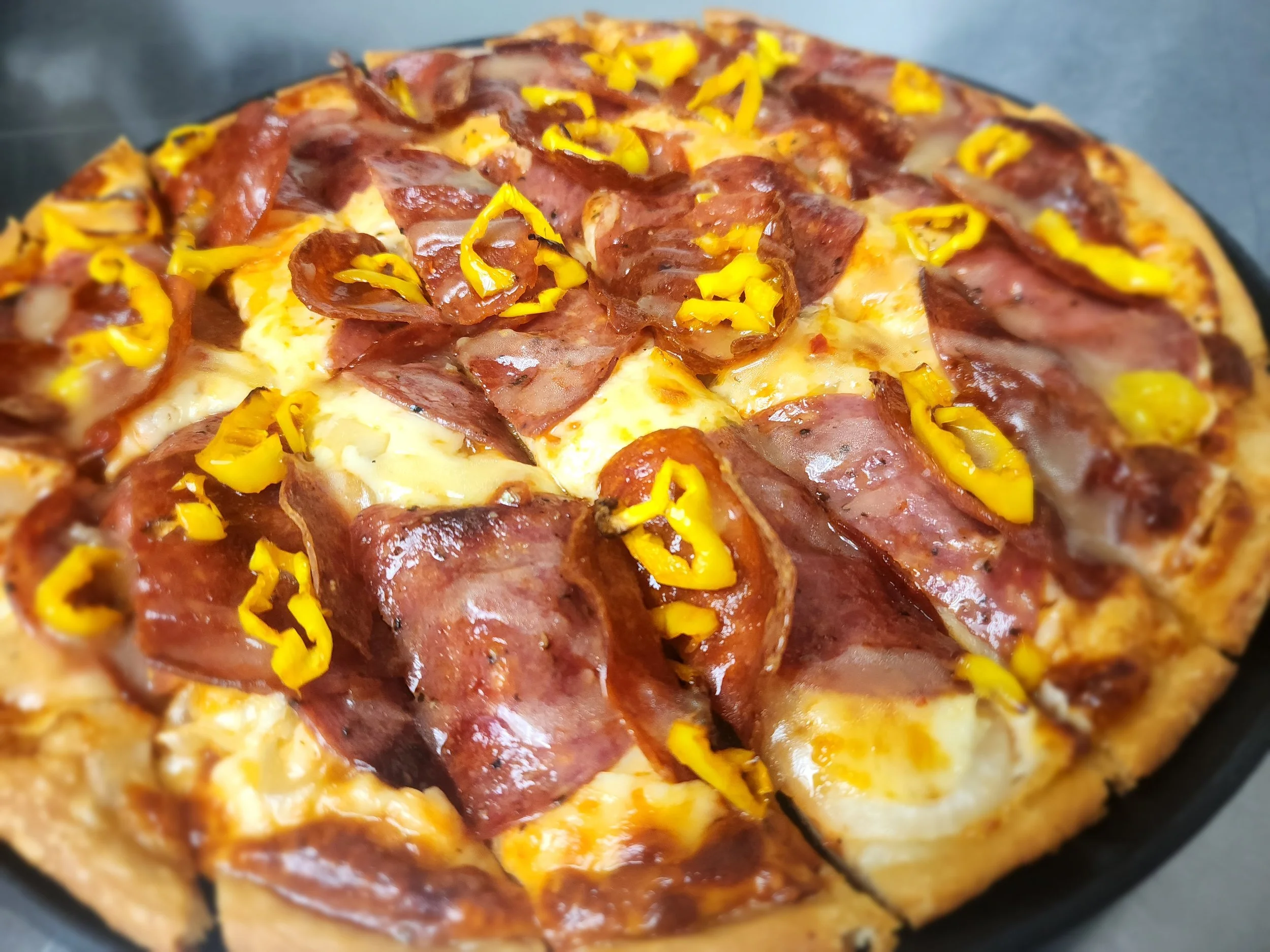 Close-up of an 'Italian Substitute' pizza topped with slices of pepperoni, salami, provolone cheese, and yellow bell peppers.
