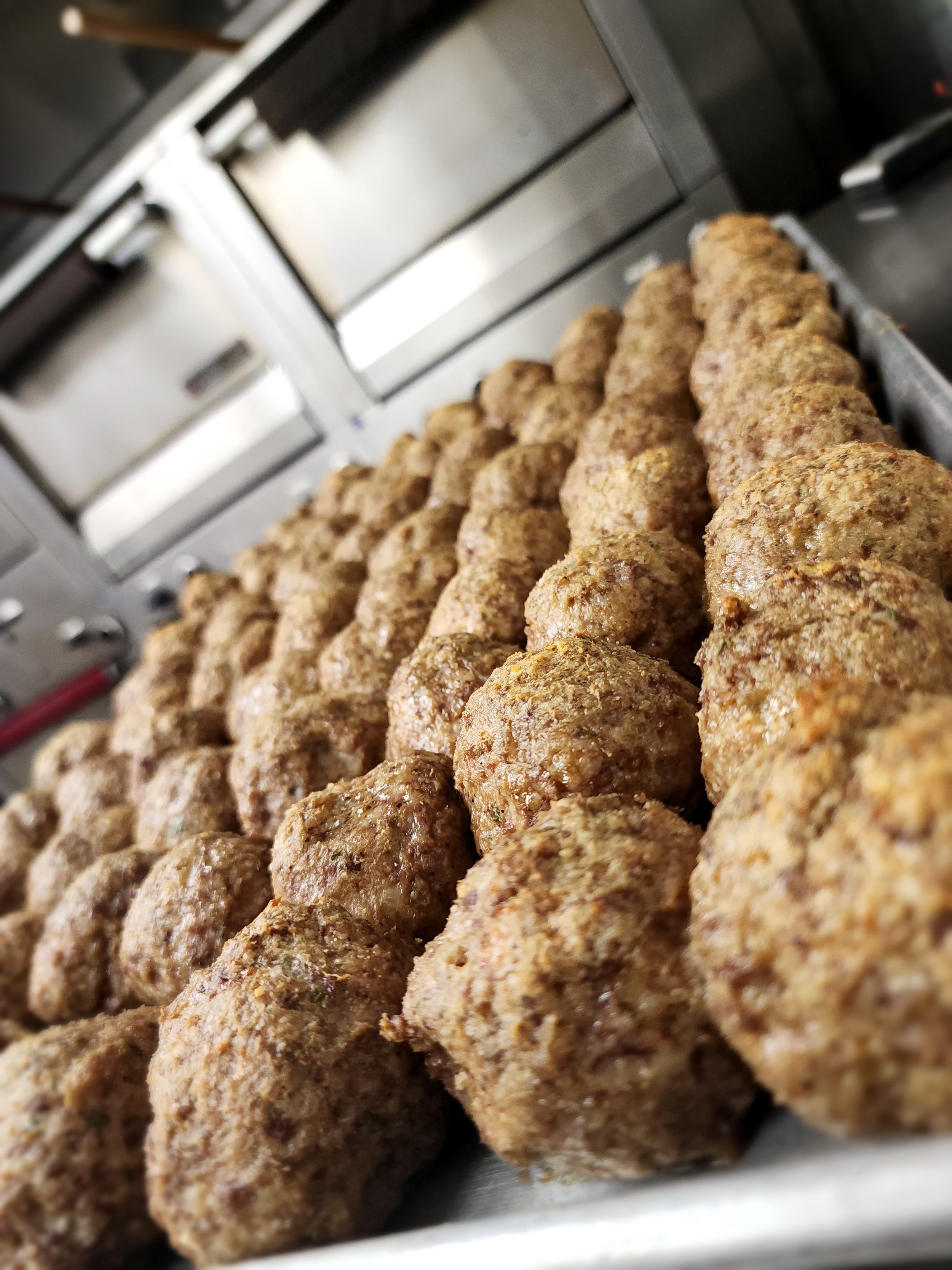 Several homemade meatballs lined up on a tray in a kitchen.