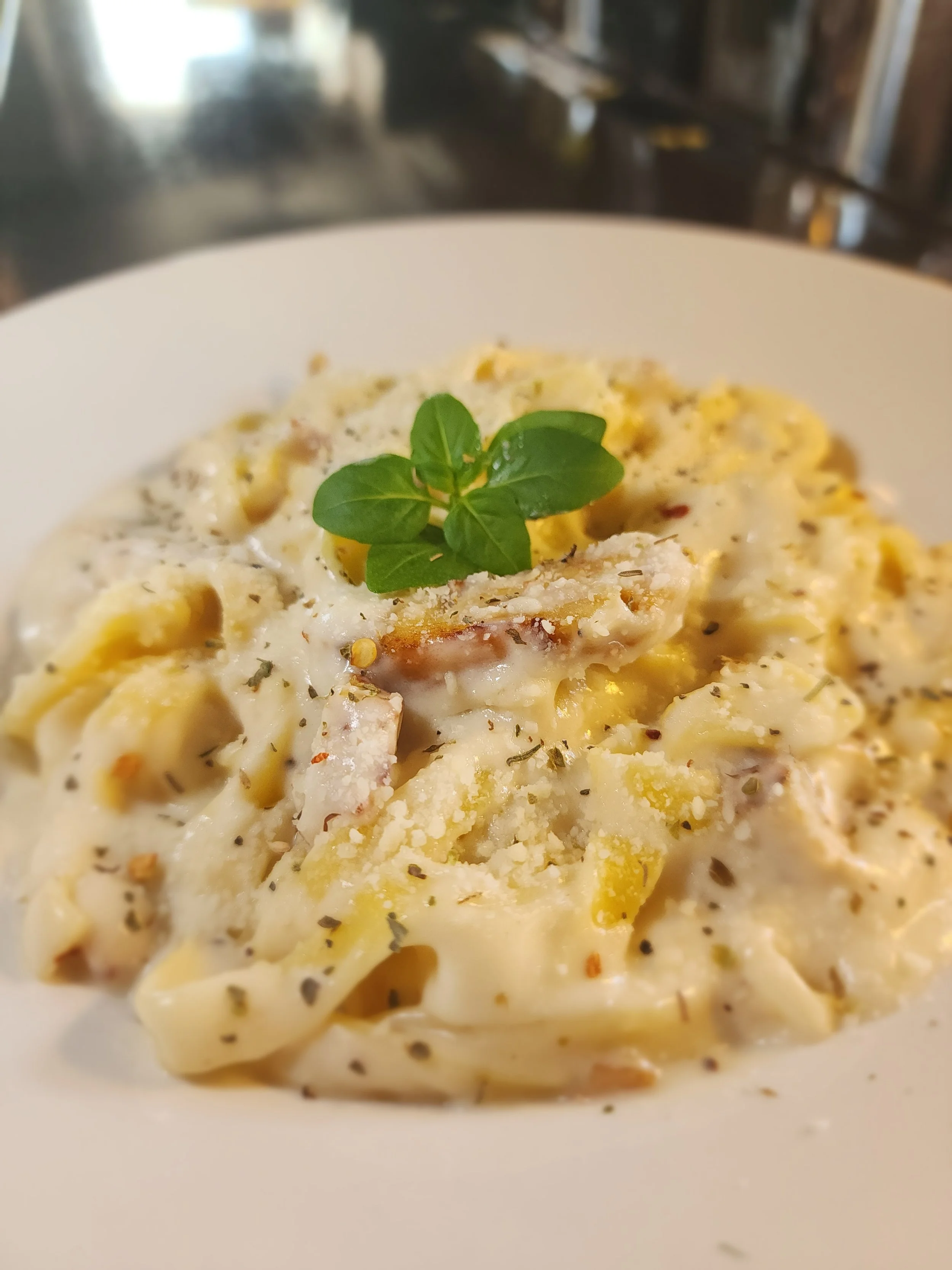 Close-up of a plate of creamy chicken alfredo garnished with a sprig of fresh basil.