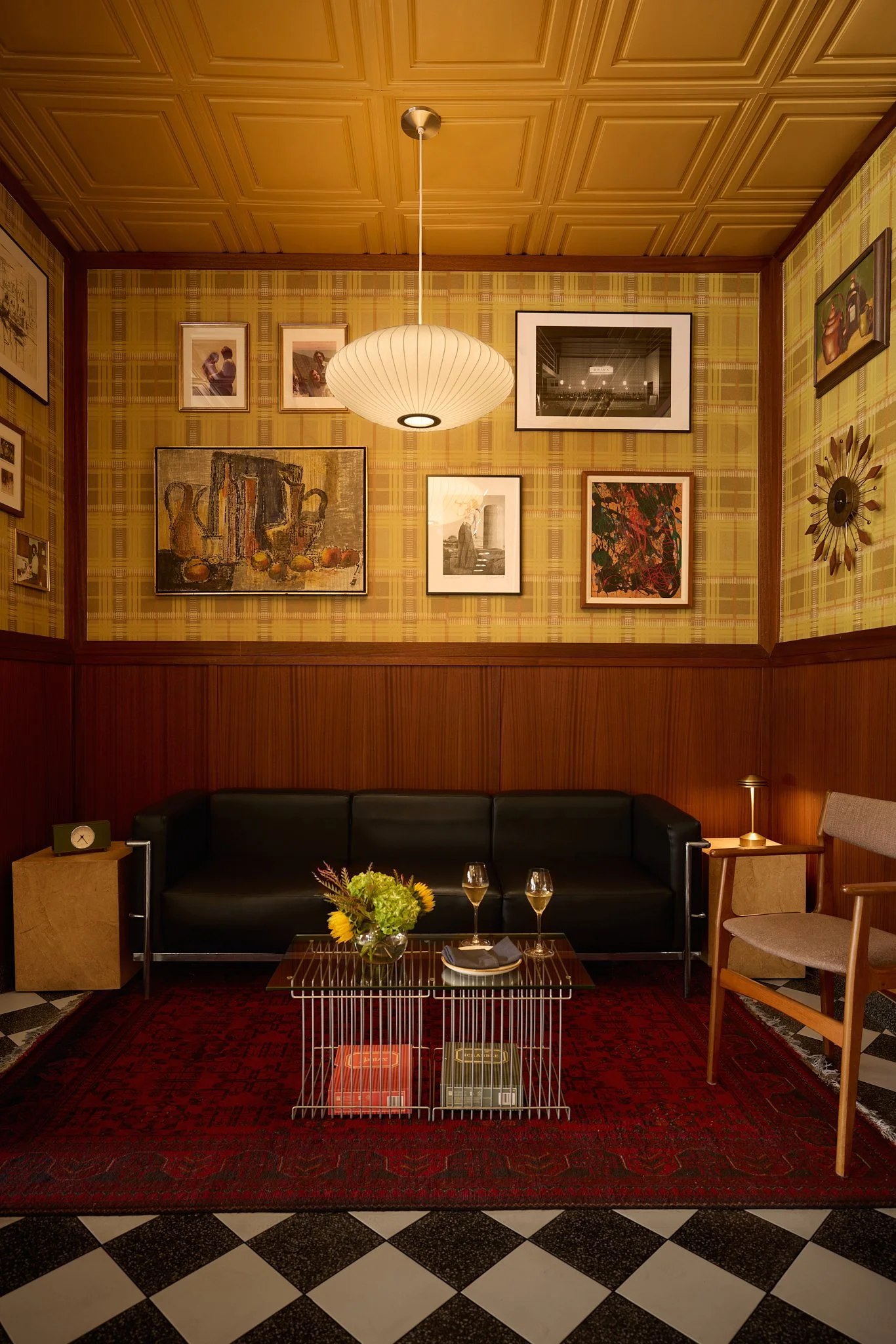 Lounge area in an Encinitas mid-century modern restaurant design project featuring wood wall paneling, vintage rug and furniture, checkered terrazzo floor tile and gallery wall.