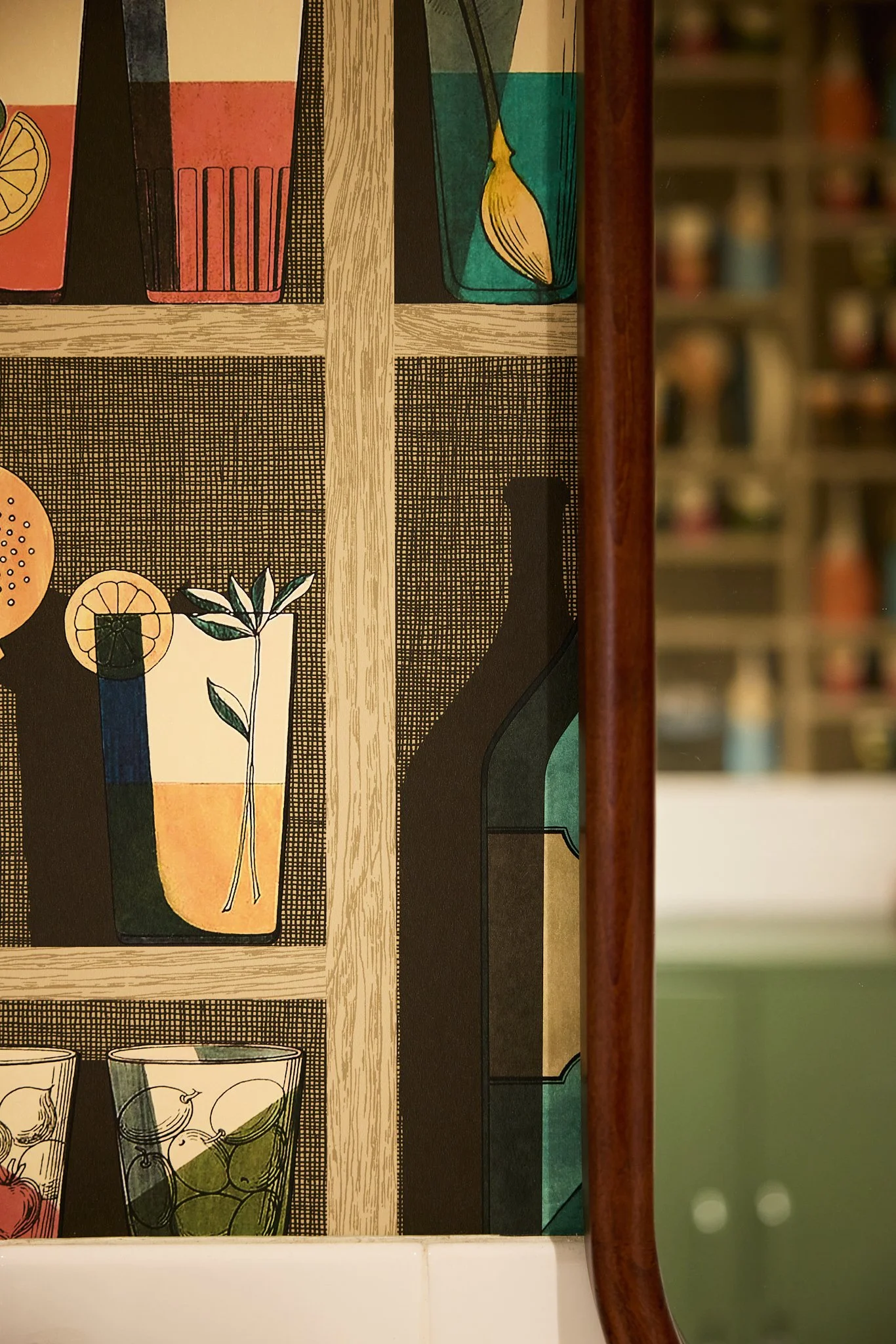 Close up of mid-century modern hospitality project bathroom in Encinitas, featuring cocktail-themed wallpaper and walnut mirror.