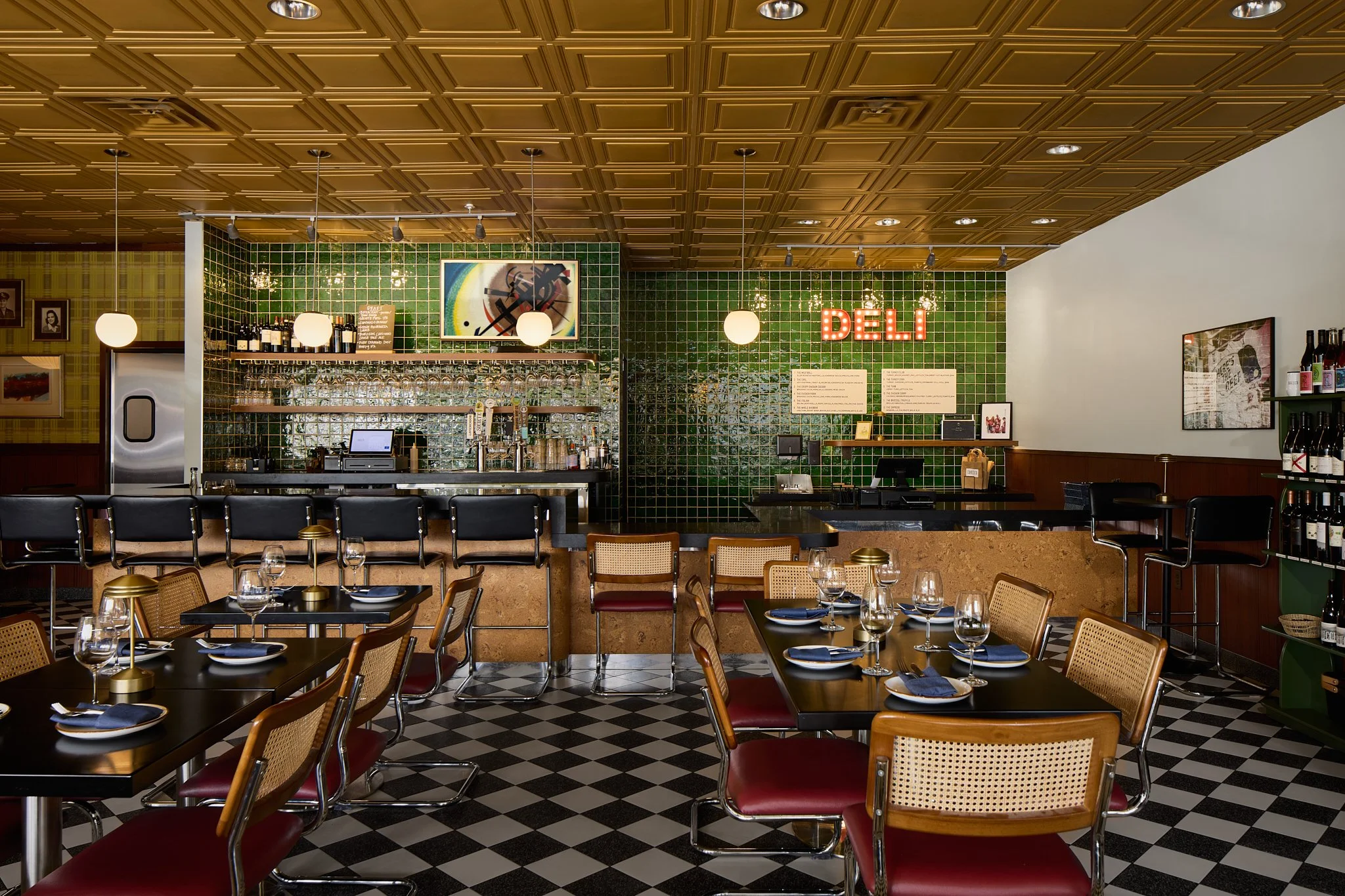 Mid-century modern wine bar and deli counter, featuring deep green wall tiles, mustard ceiling tiles, checkered terrazzo floor tiles and cork and chrome accented bar.