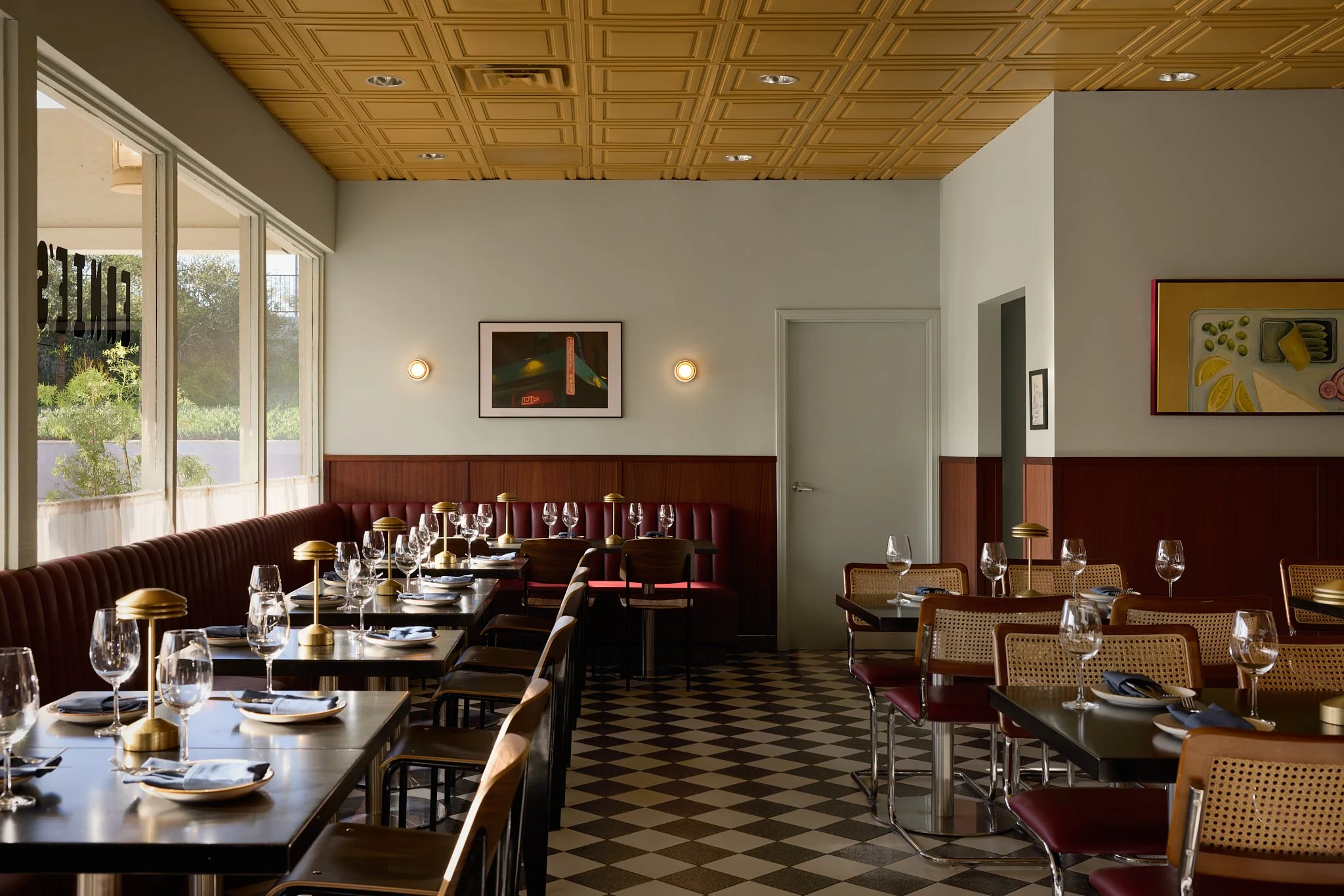 Mid-century modern restaurant dining room in Encinitas, featuring custom leather banquette seating, wood wall paneling, brass table lighting, mustard ceiling tiles and terrazzo floor tiles.