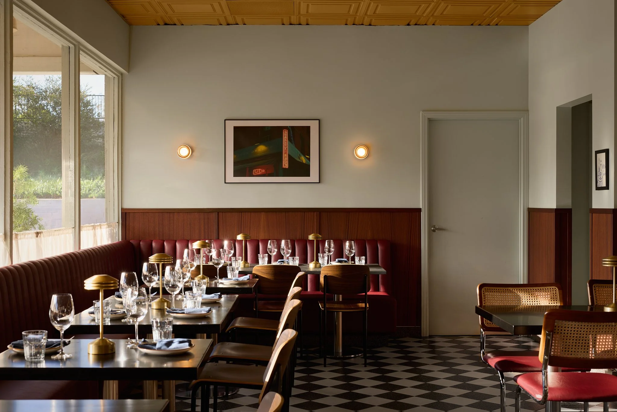 Mid-century modern Encinitas restaurant and wine bar dining room featuring checkered terrazzo floor tiles, custom leather banquette, wood wall paneling and brass table lamps.