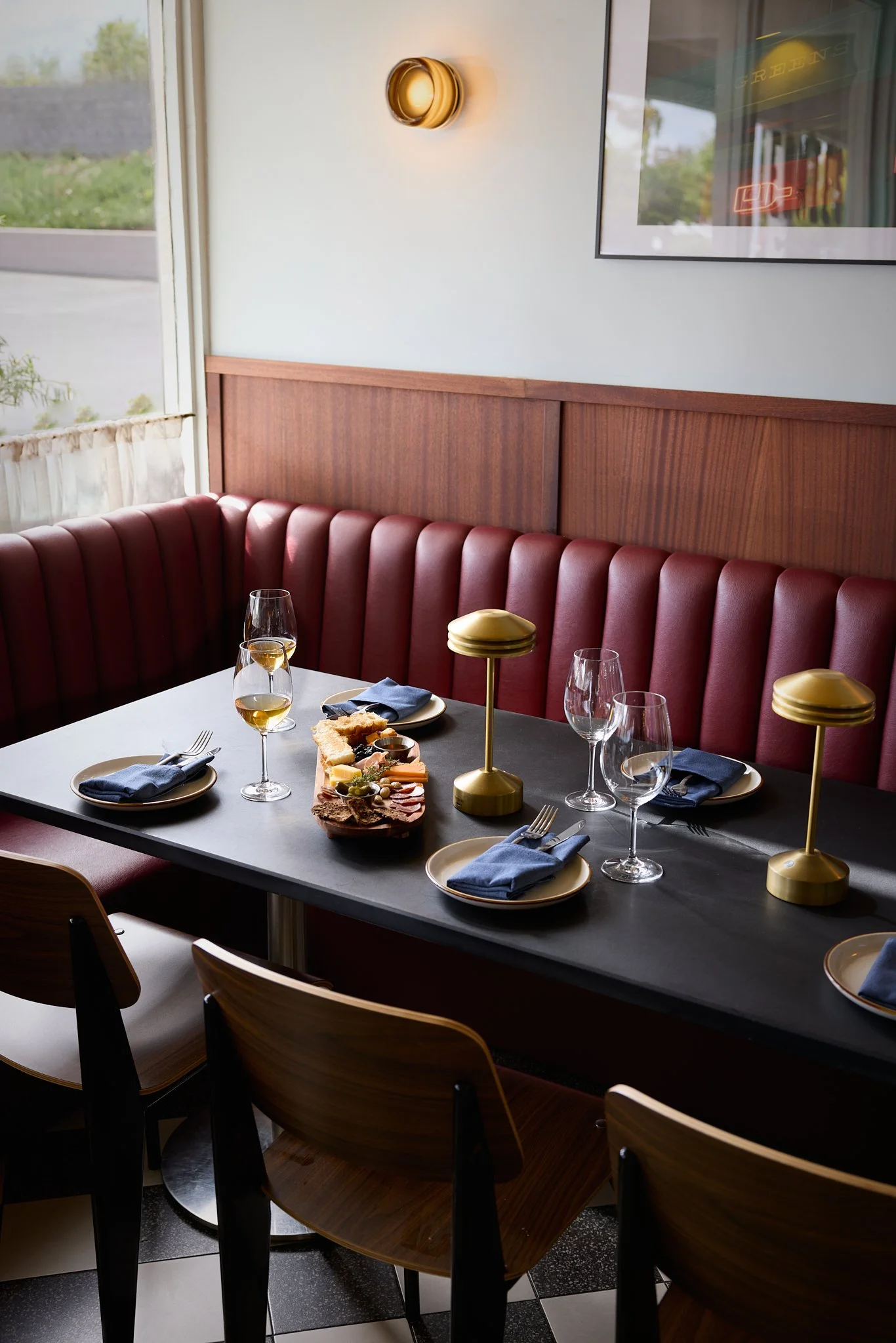 Close up of mid-century modern style banquette dining area featuring custom leather bench seating, vintage style chairs, brass table lamps and wood wall paneling.