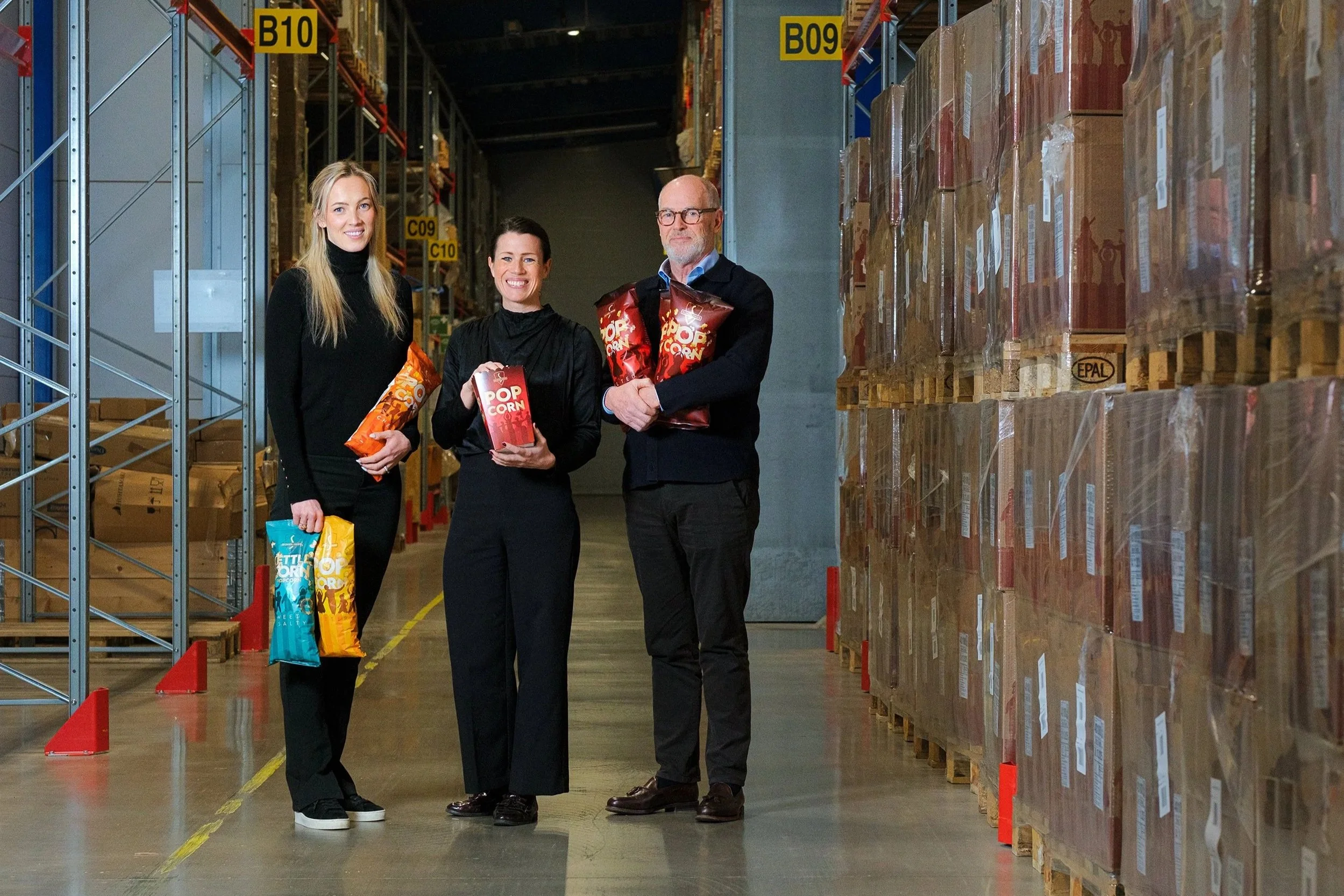 Tre personer i ett lager eller lagerlokal som håller popcornpåsar.