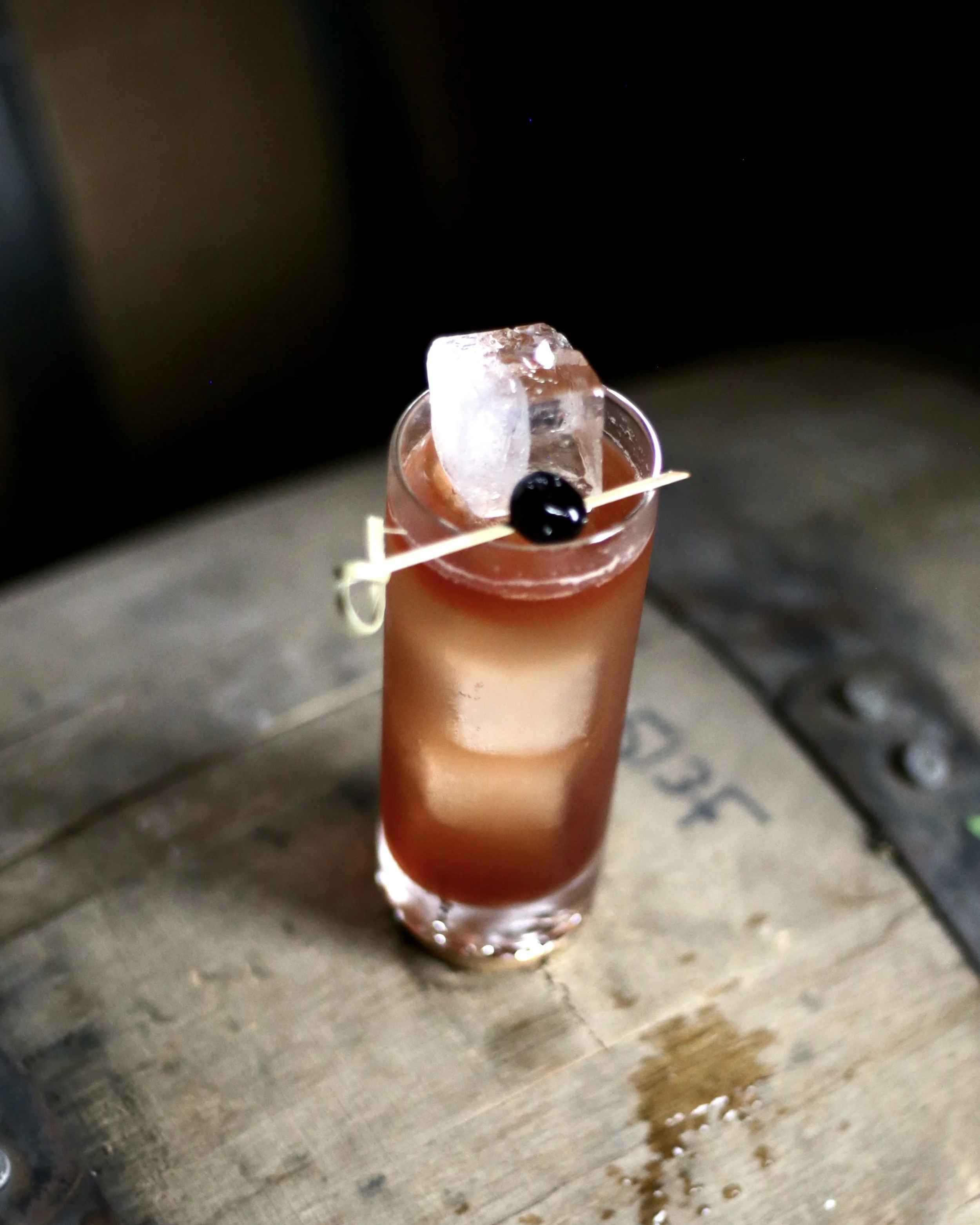 A close-up of a Horsefeather cocktail, a whiskey highball served in a tall glass sitting on a wooden surface.