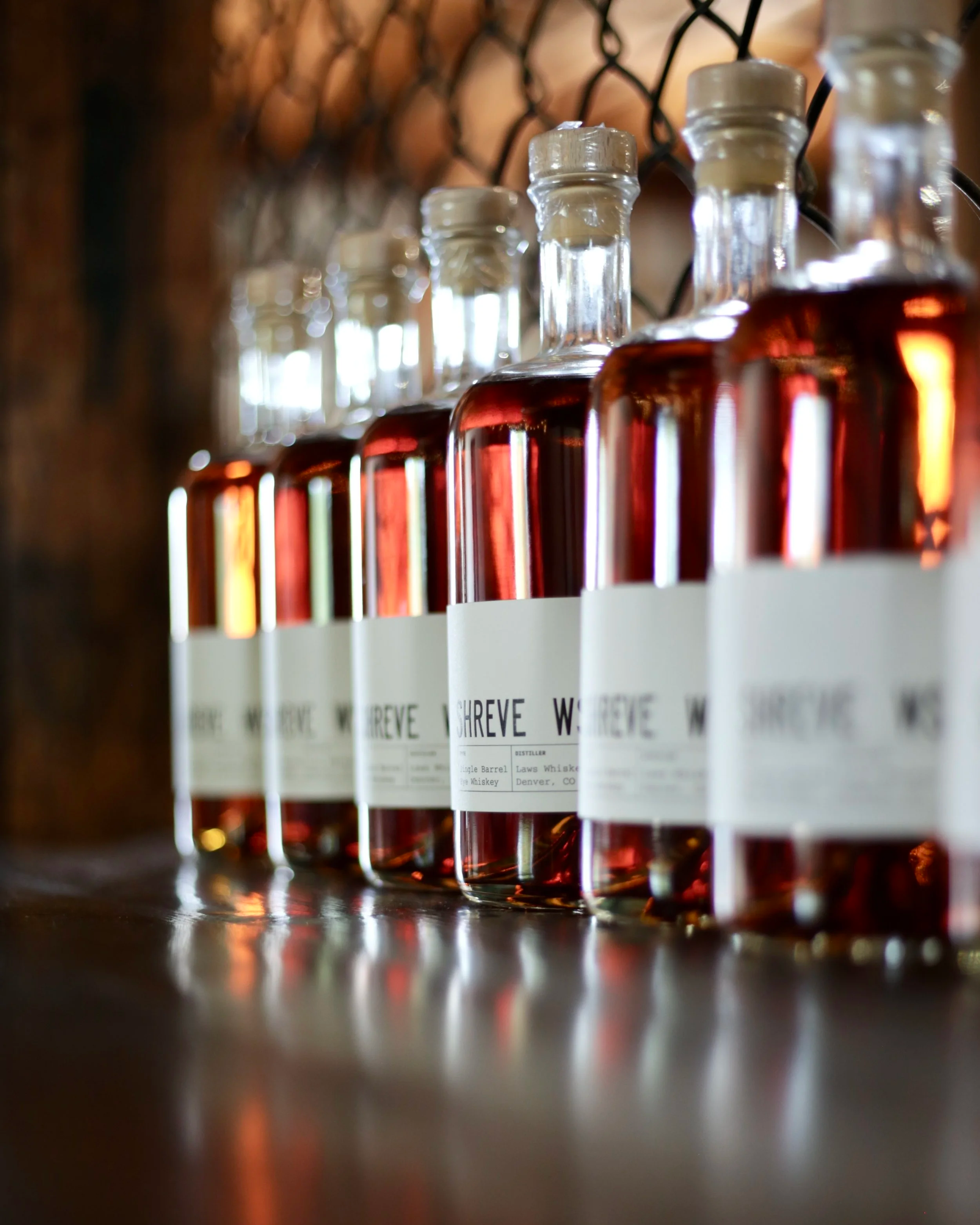 Close-up of several glass bottles with cork stoppers, filled with amber-colored whiskey, standing in a row on top of a bar.