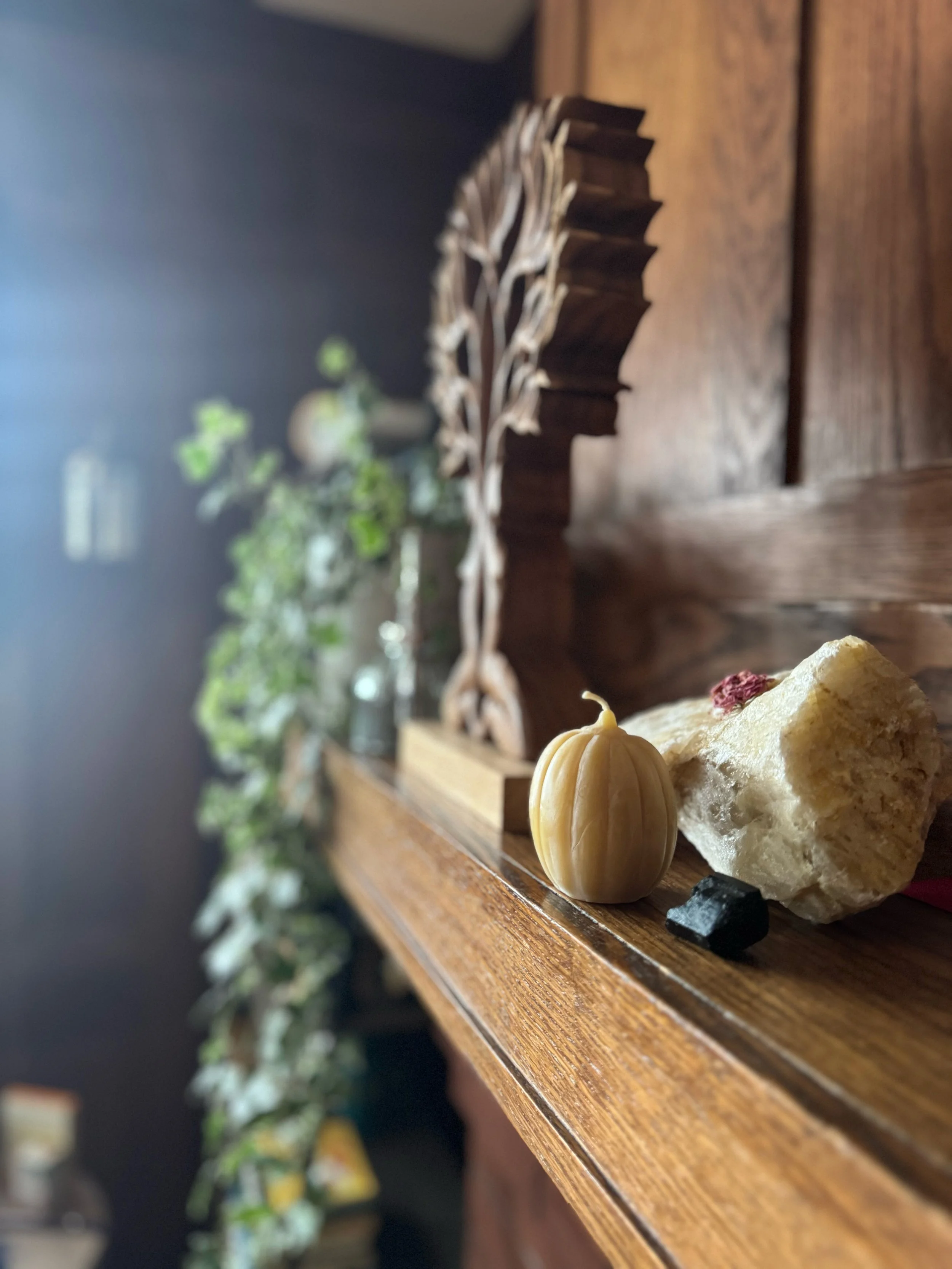 Decorative display on a wooden surface with a small gourd, a piece of sponge cake, and small stones, with blurred greenery and a wooden sculpture in the background.