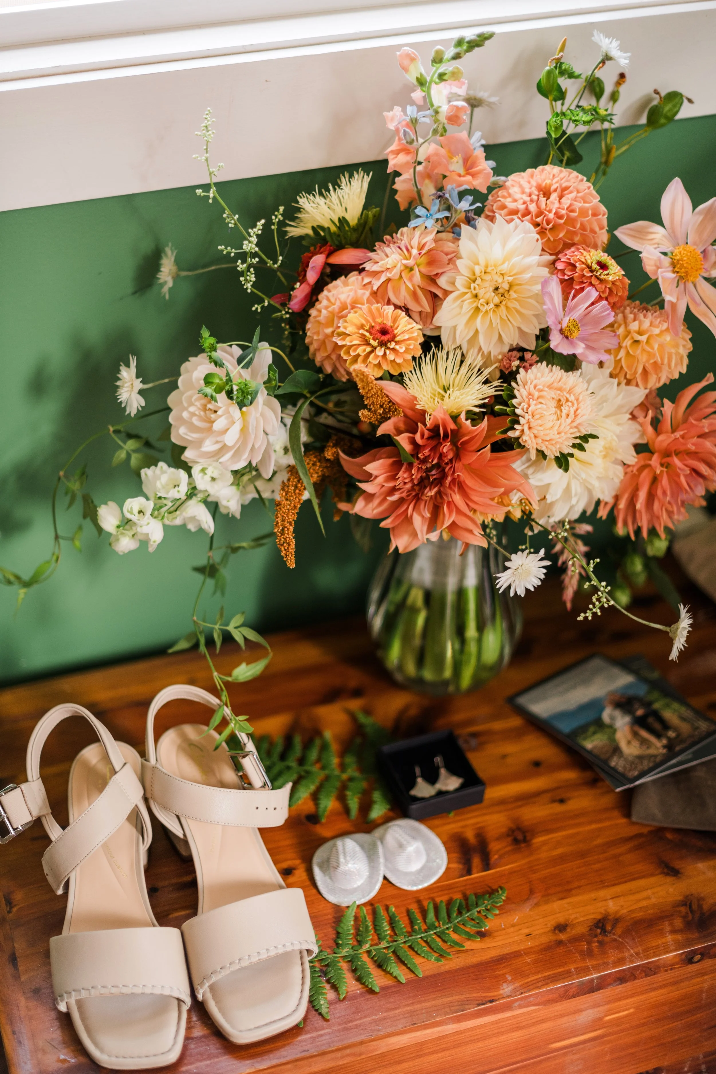 Bridal bouquet with bride's shoes, earrings, and cufflinks. Bridal bouquet is lush and flowing with warm orange and light yellow dahlia and arching hops and jasmine vines.