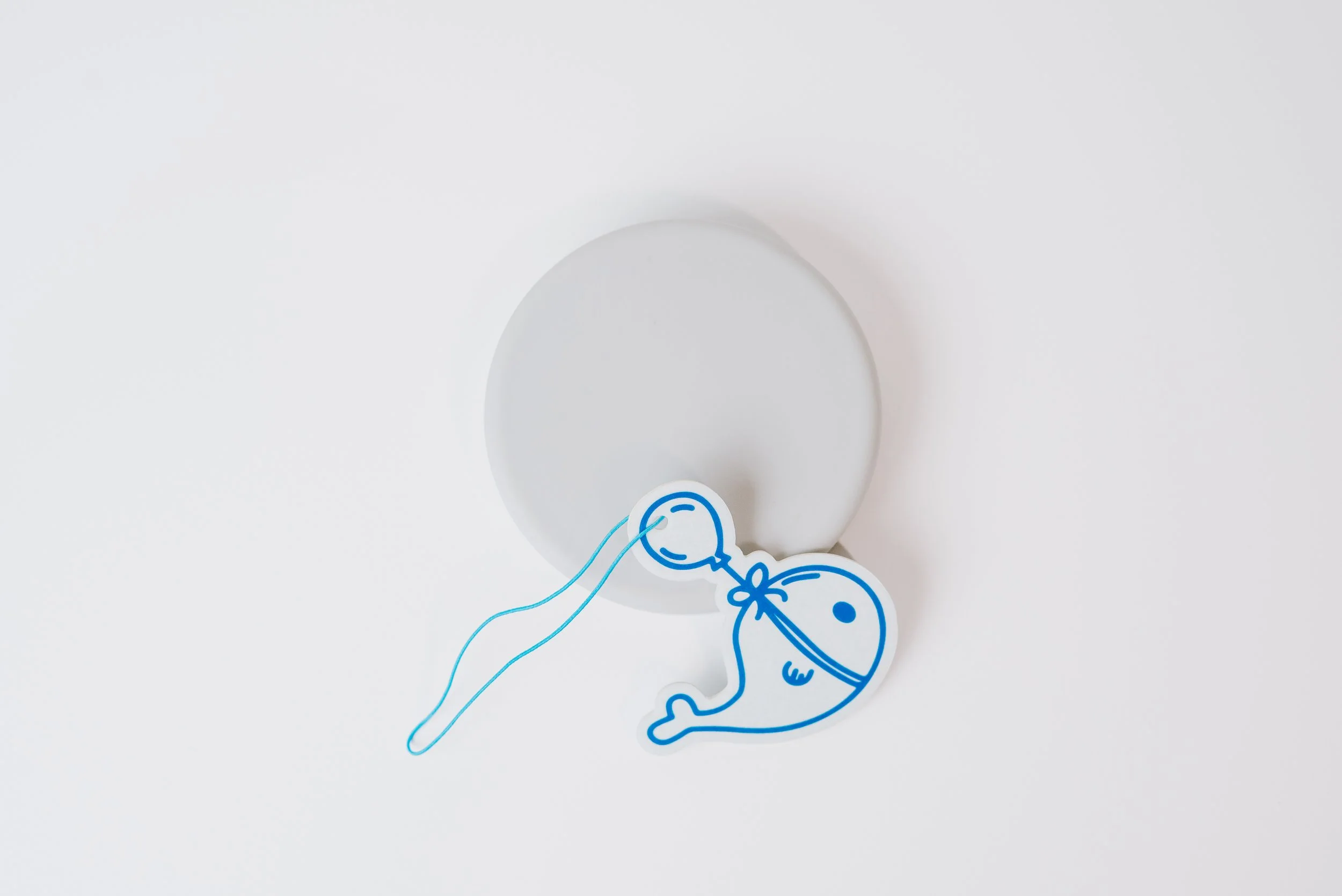 A white circular object with a blue line drawing of a baby sleeping, attached to a blue string, on a plain white background.