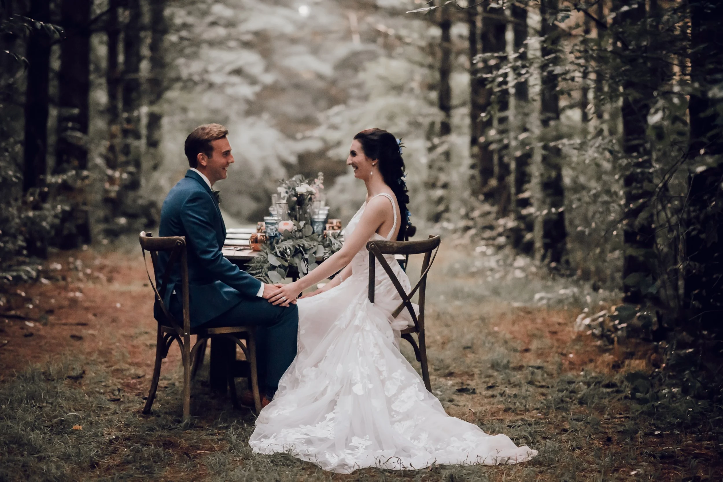 A bride and groom sit at a private table in the woods, at their luxurious, rustic wedding planned by bella and fern event planning.