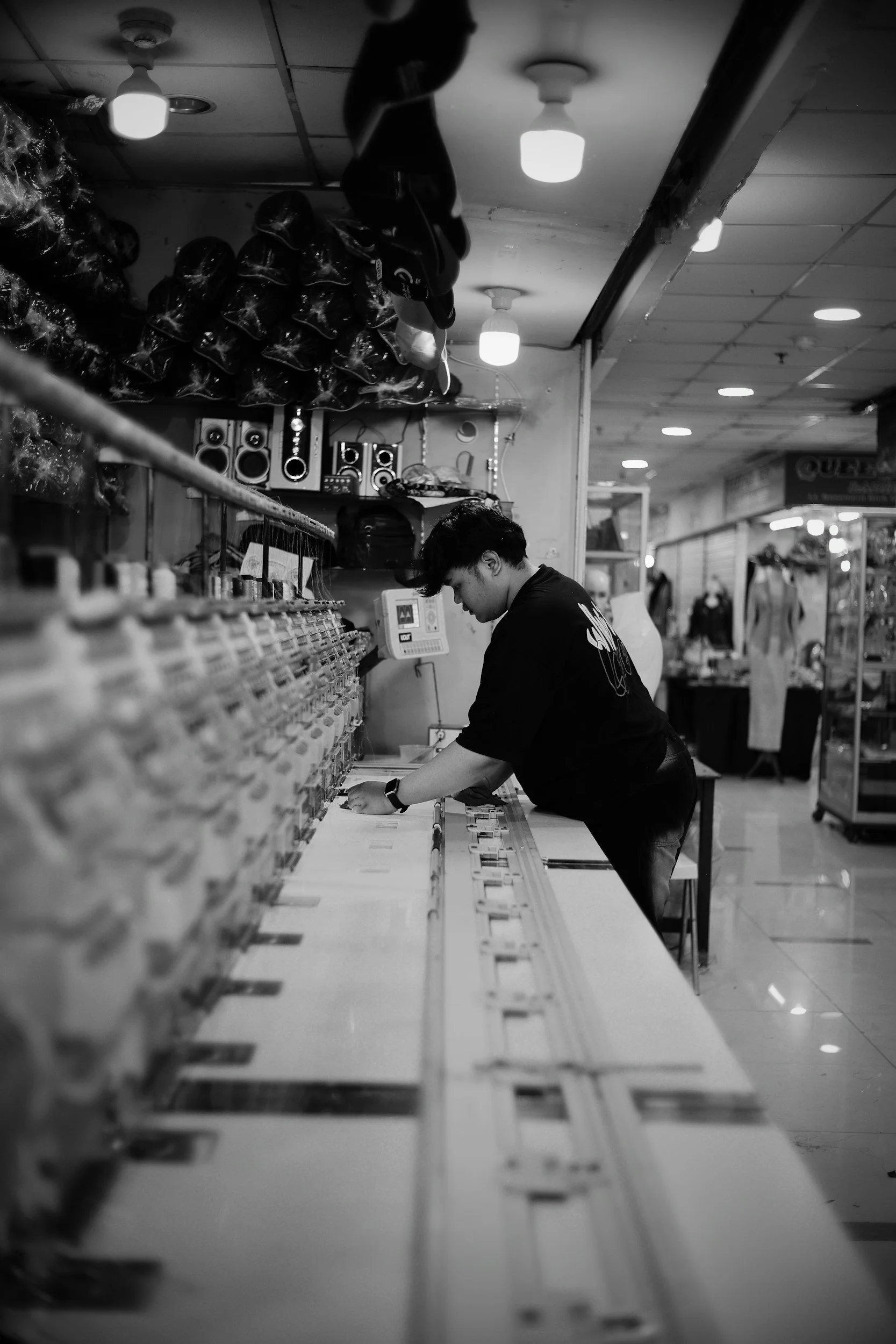 A young man working at a record store, selecting vinyl records from a shelf, with stacked headphones and speakers in the background.